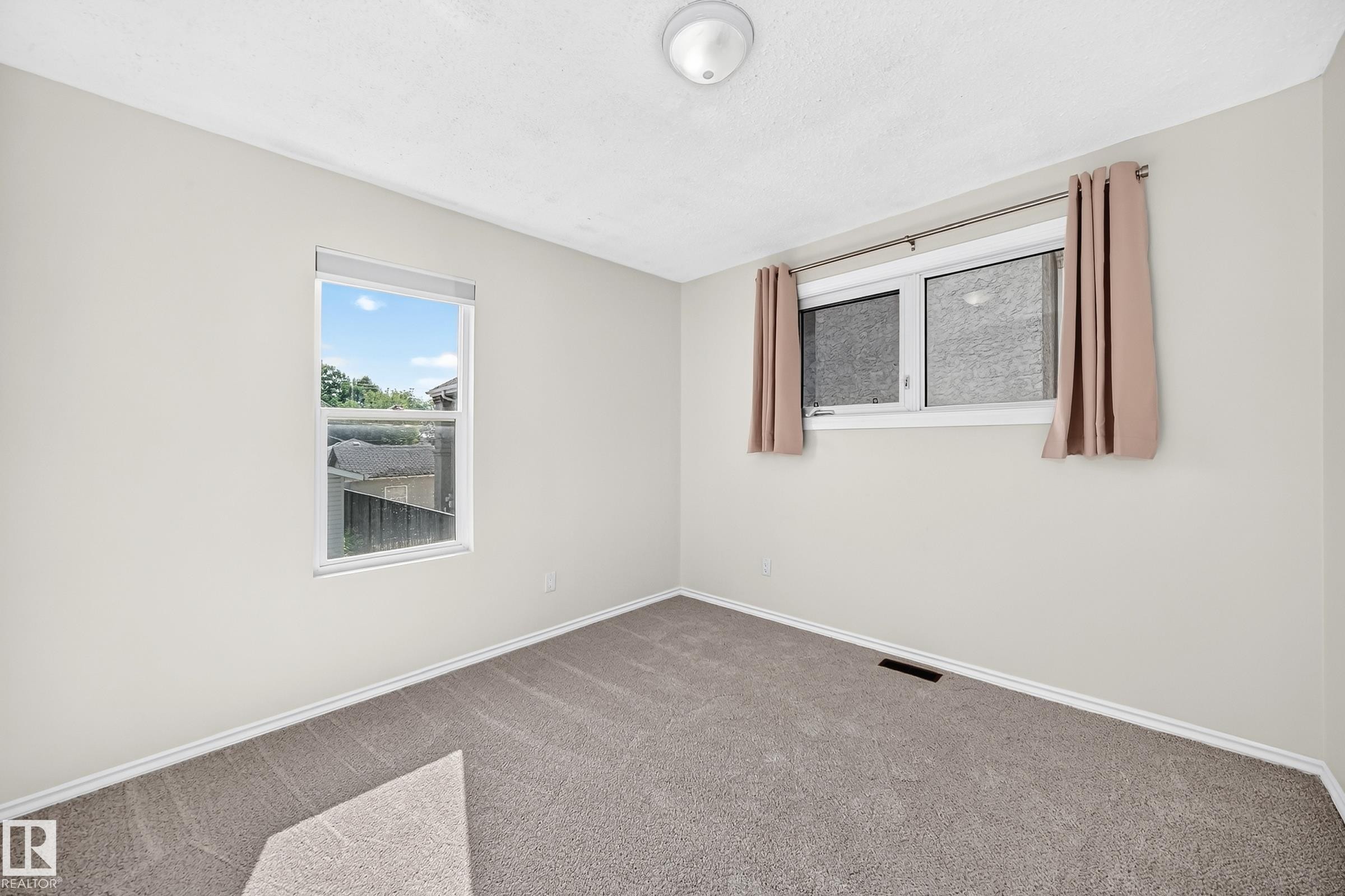 Neutral wall color, two windows, carpeted flooring, and a ceiling-mounted light fixture - 12721 117 Street Nw, Edmonton, AB