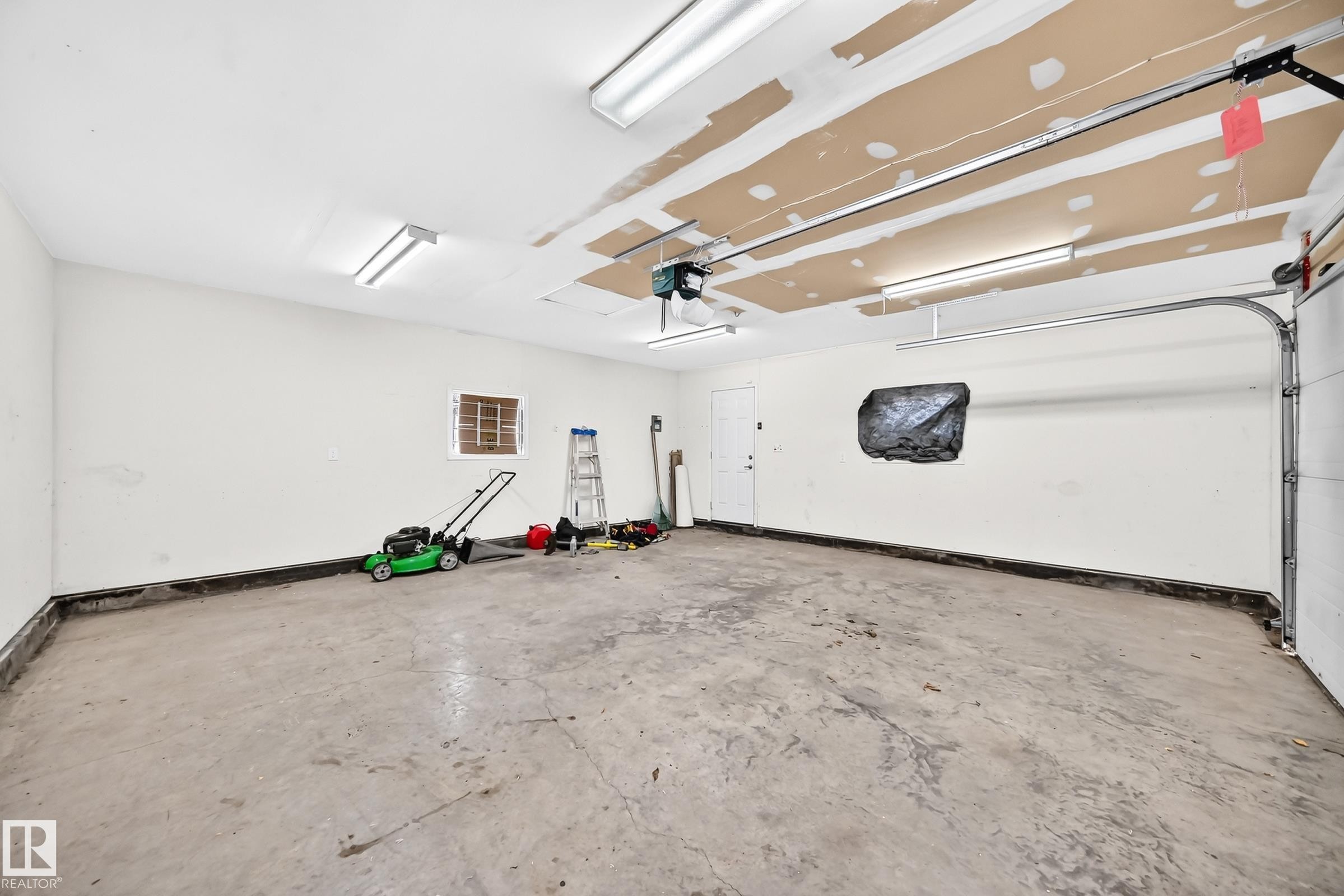 Concrete flooring garage with an interior access door, multiple fluorescent light fixtures, and a garage door track system - 12721 117 Street Nw, Edmonton, AB