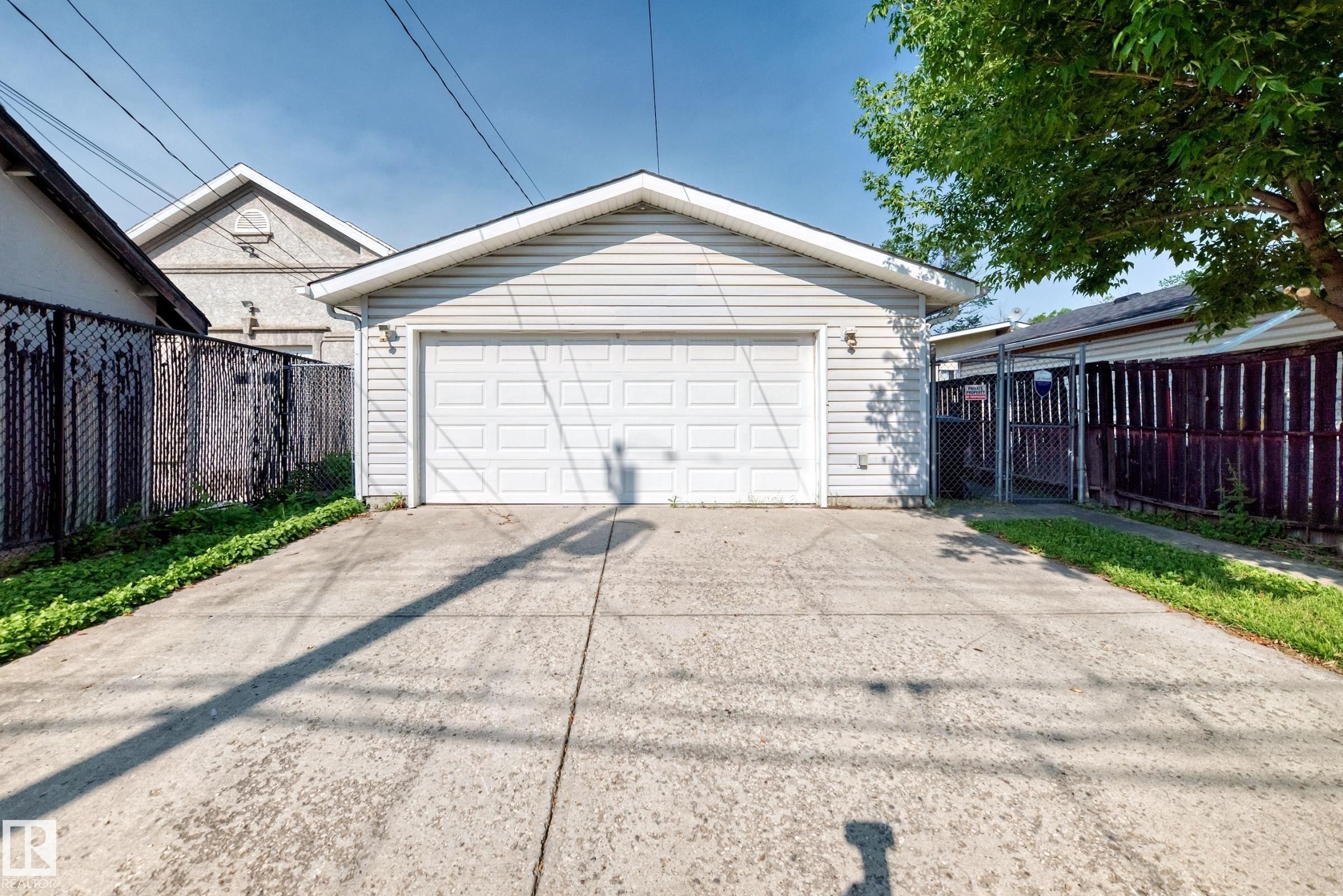 Two-car garage with a paneled door, exterior wall lighting, and concrete driveway - 12721 117 Street Nw, Edmonton, AB