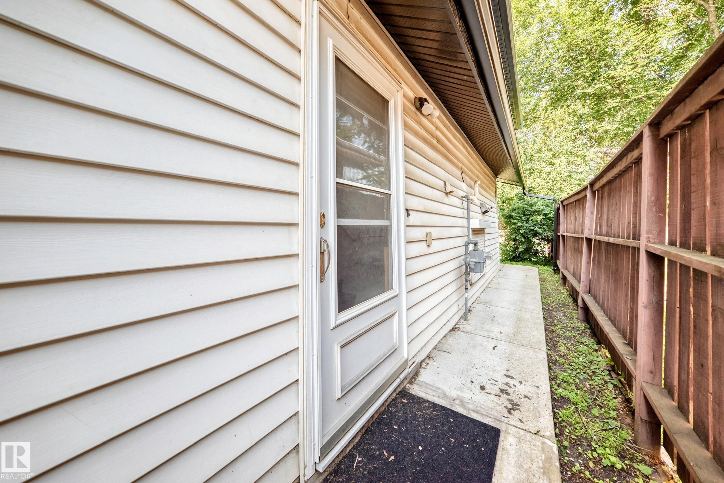 White siding exterior with a screen door, concrete pathway, and wood privacy fence - 12721 117 Street Nw, Edmonton, AB