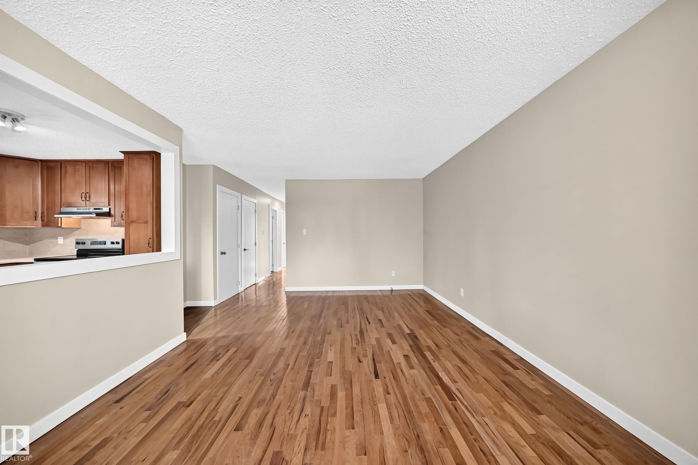 Hardwood flooring throughout, kitchen with wood cabinetry, stainless steel range, and track lighting, and a neutral wall palette - 12721 117 Street Nw, Edmonton, AB