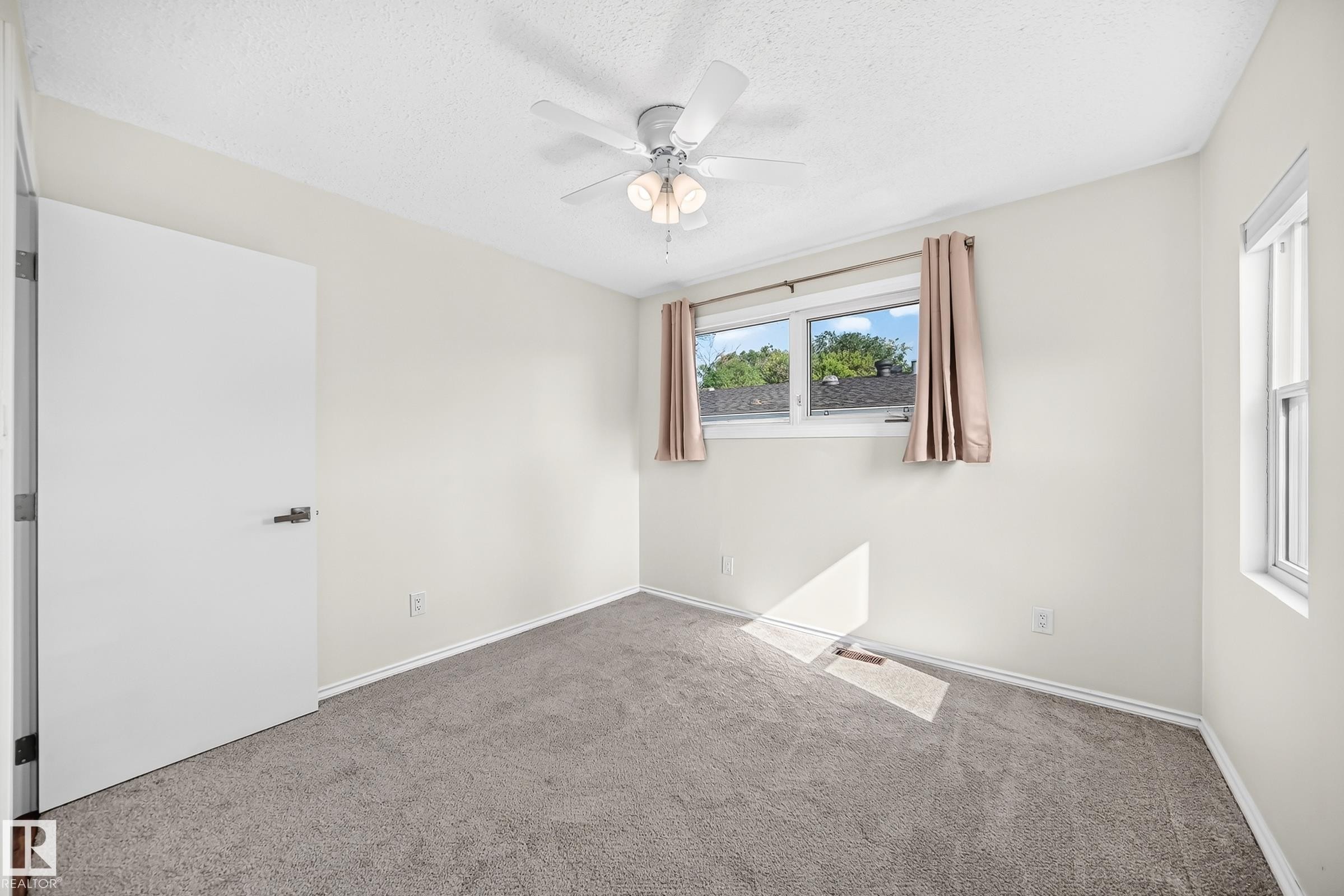 Wall-to-wall carpeting, ceiling fan with integrated lighting, multiple windows providing natural light, and a flat-panel interior door with dark hardware - 12721 117 Street Nw, Edmonton, AB