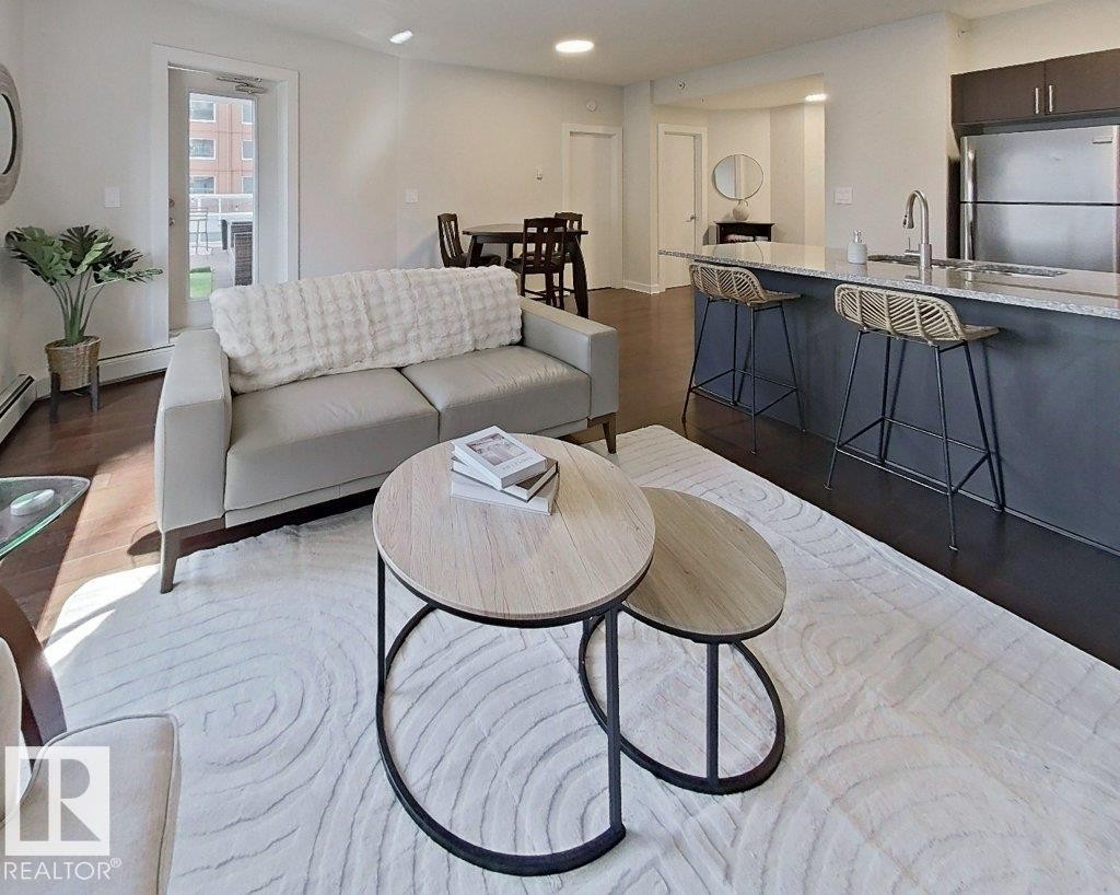 Open concept living area featuring dark wood-finish flooring, a kitchen island with seating, stainless steel appliances, and a glass-paneled exterior door - #605 10152 104 St Nw, Edmonton, AB