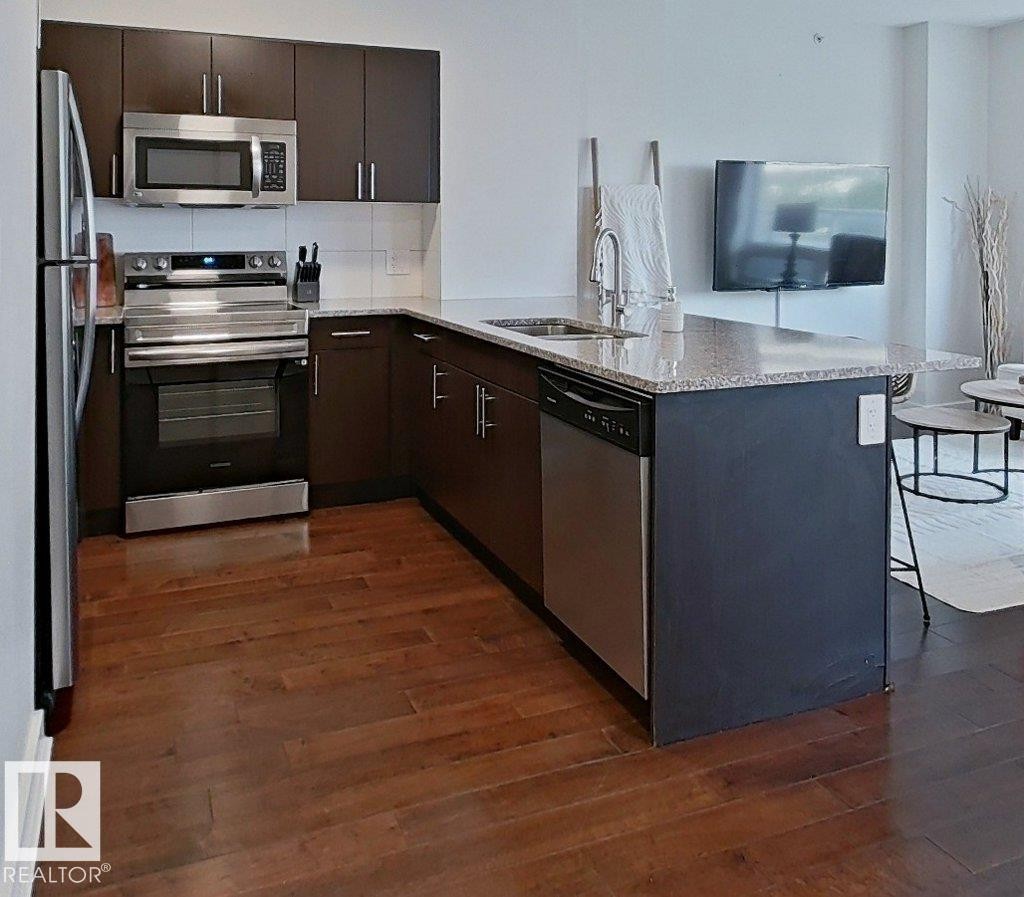Kitchen featuring wood-finish flooring, stainless steel appliances, dark wood-finish cabinetry, and a light-toned countertop - #605 10152 104 St Nw, Edmonton, AB
