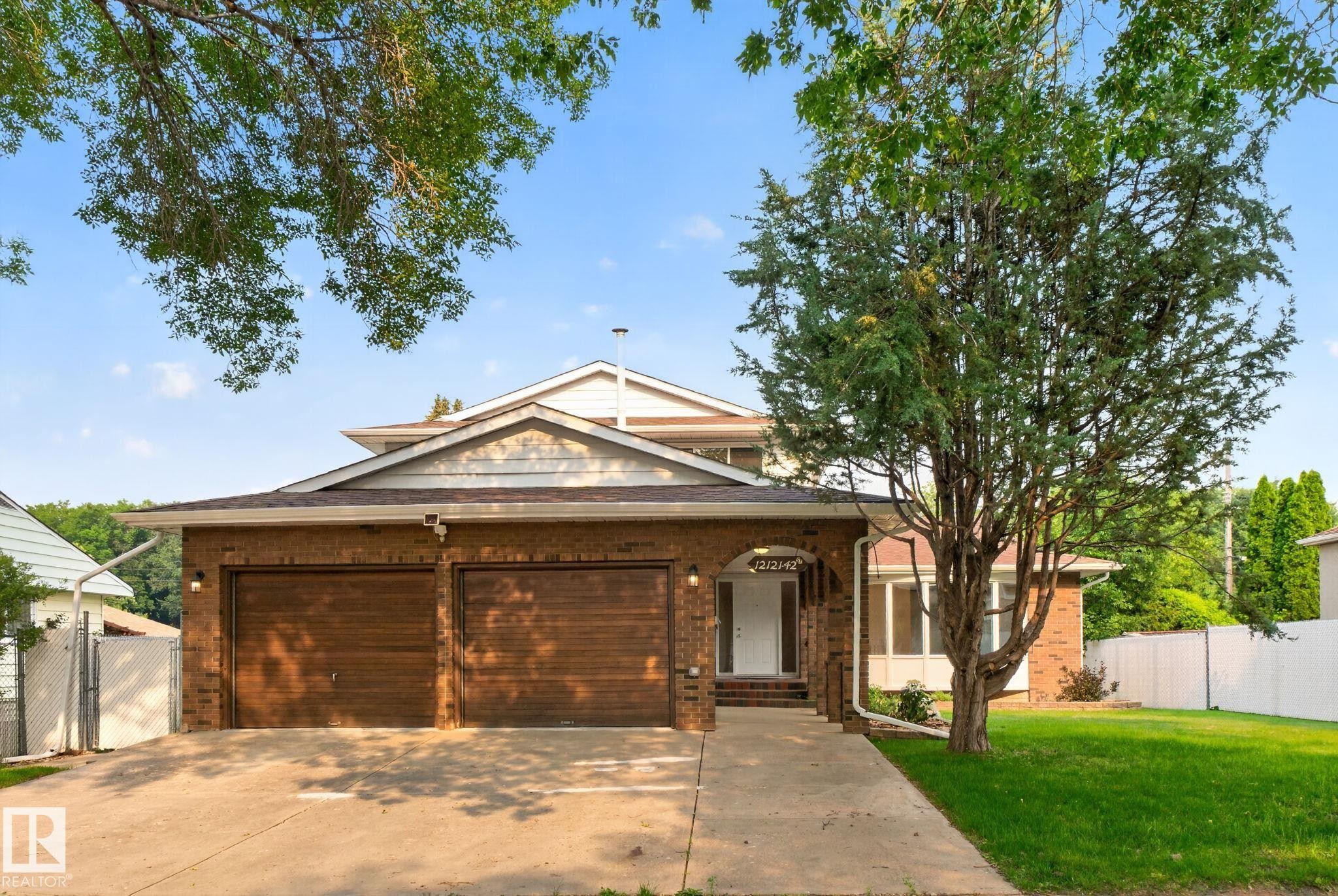 Brick exterior featuring a two-car garage with wood-finish doors - 12121 42 Street Nw, Edmonton, AB - Outdoor