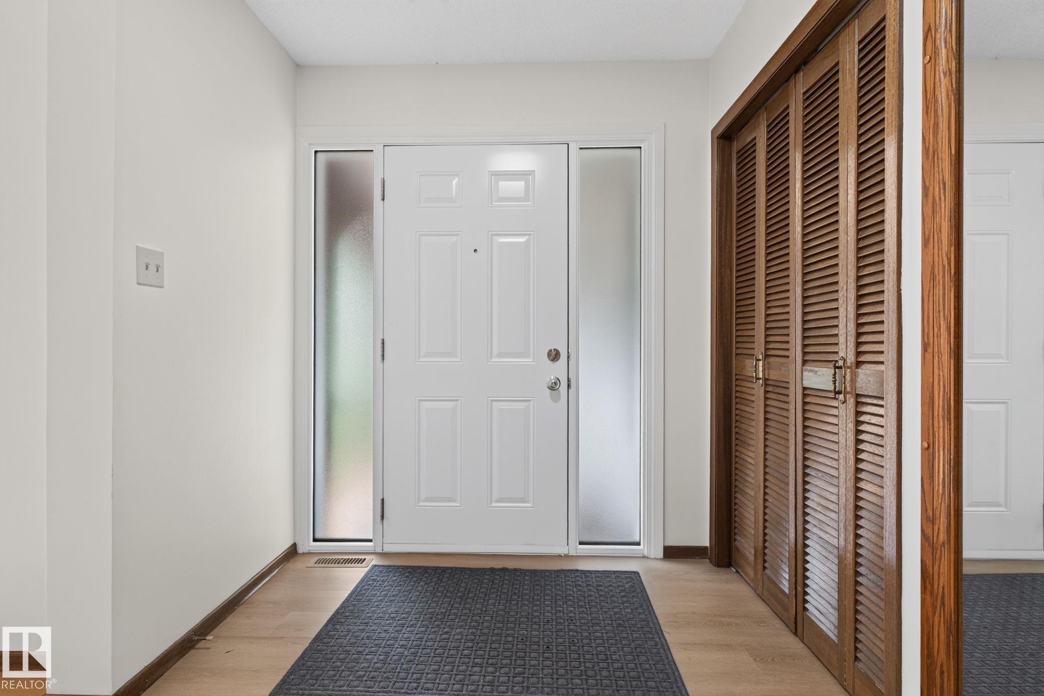Entryway featuring a white paneled door with frosted sidelights, wood-finish flooring, and a louvered bi-fold closet - 12121 42 Street Nw, Edmonton, AB - Indoor Photo Showing Other Room