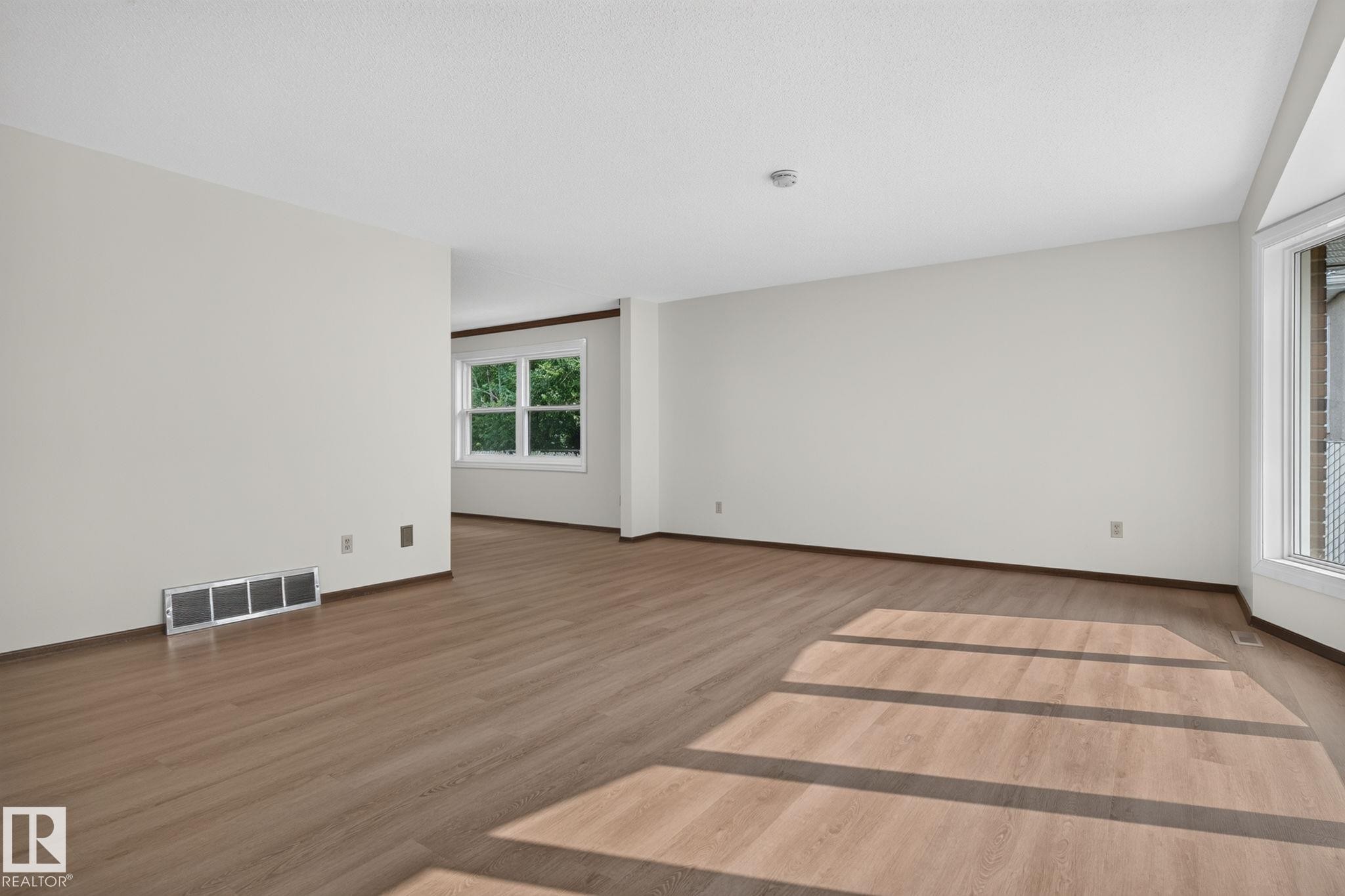 Spacious room featuring wood-finish flooring, white walls, and white trim - 12121 42 Street Nw, Edmonton, AB - Indoor Photo Showing Other Room