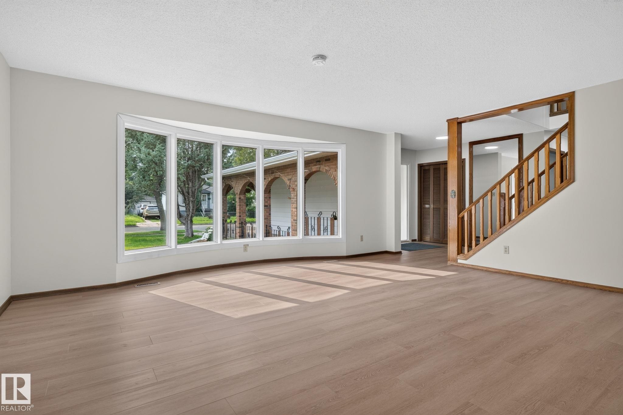 Expansive living area featuring a curved bay window, wood-finish flooring, and a hardwood staircase - 12121 42 Street Nw, Edmonton, AB - Indoor
