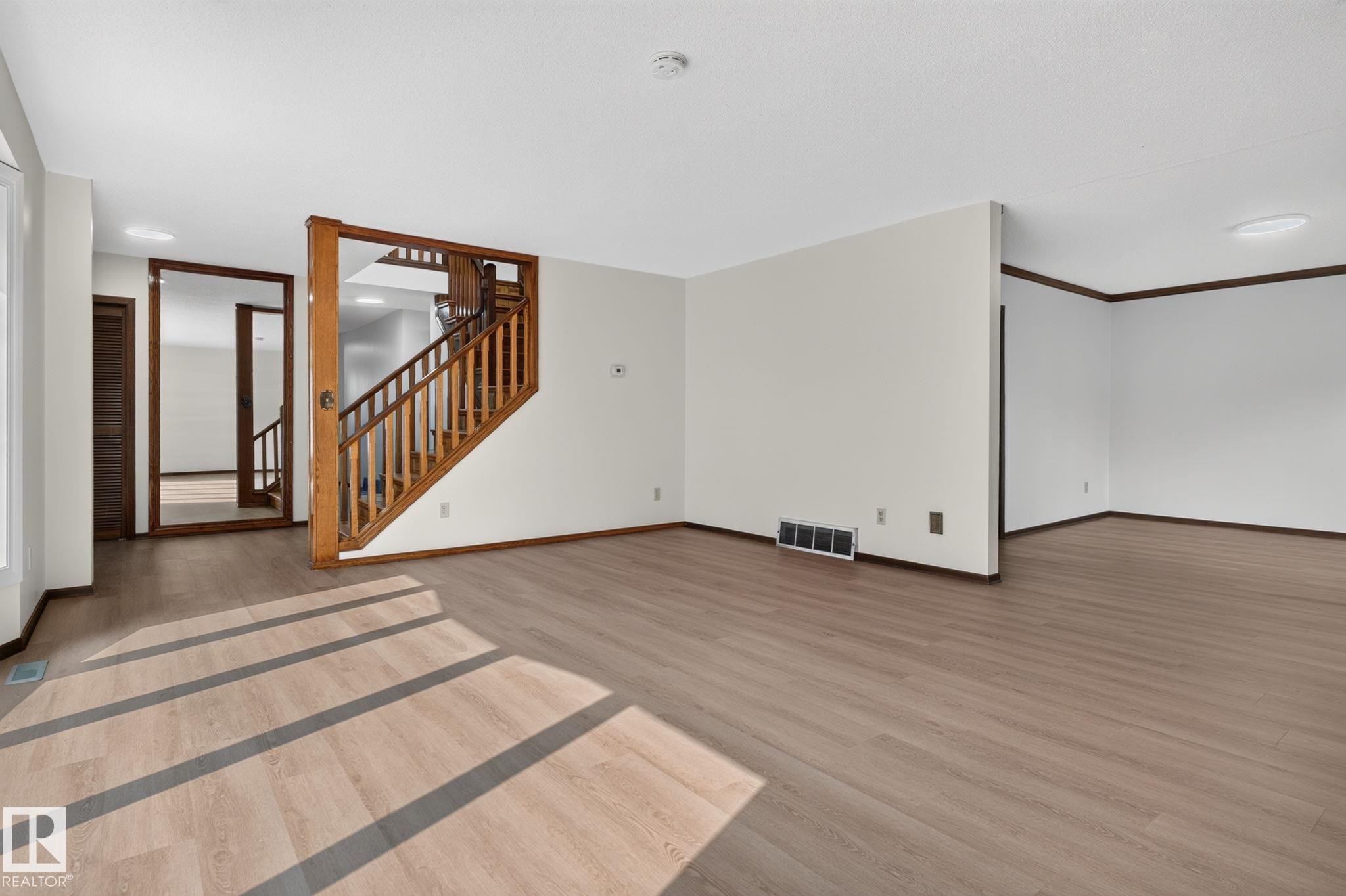 Open concept living area featuring wood-finish flooring, white walls, and a prominent wooden staircase with matching banister - 12121 42 Street Nw, Edmonton, AB - Indoor Photo Showing Other Room