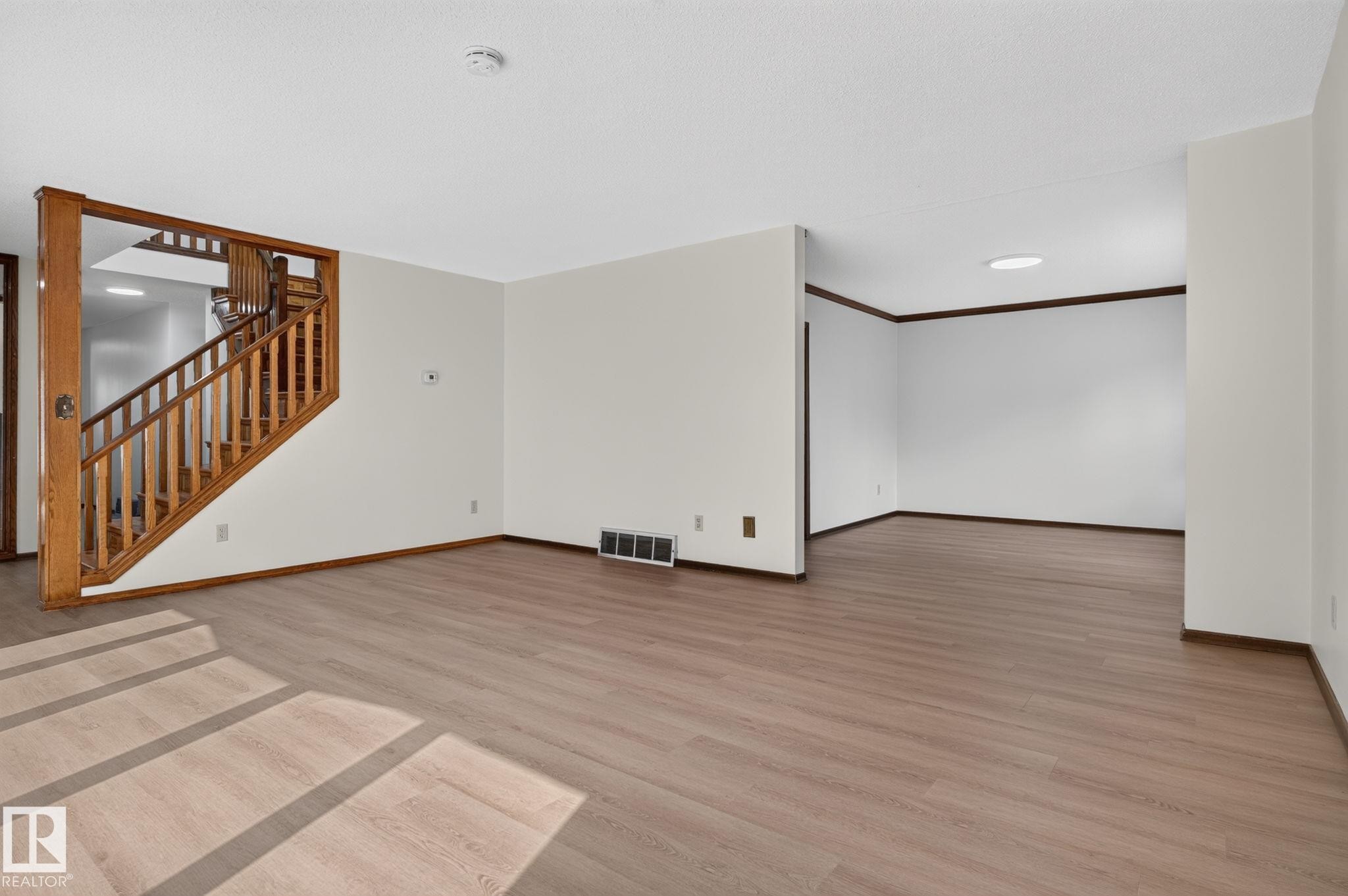 Spacious interior featuring wood-finish flooring, a wood staircase with balusters, light-toned walls, and a ceiling light fixture - 12121 42 Street Nw, Edmonton, AB - Indoor Photo Showing Other Room