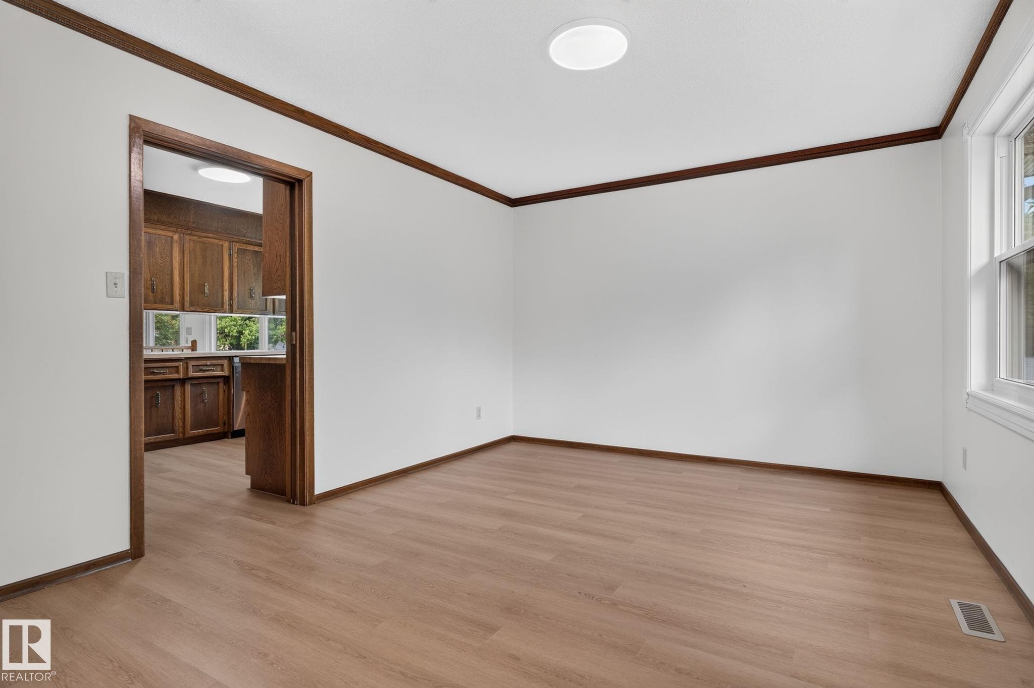 Bright room with wood-finish flooring, white walls, and dark wood trim - 12121 42 Street Nw, Edmonton, AB - Indoor Photo Showing Other Room