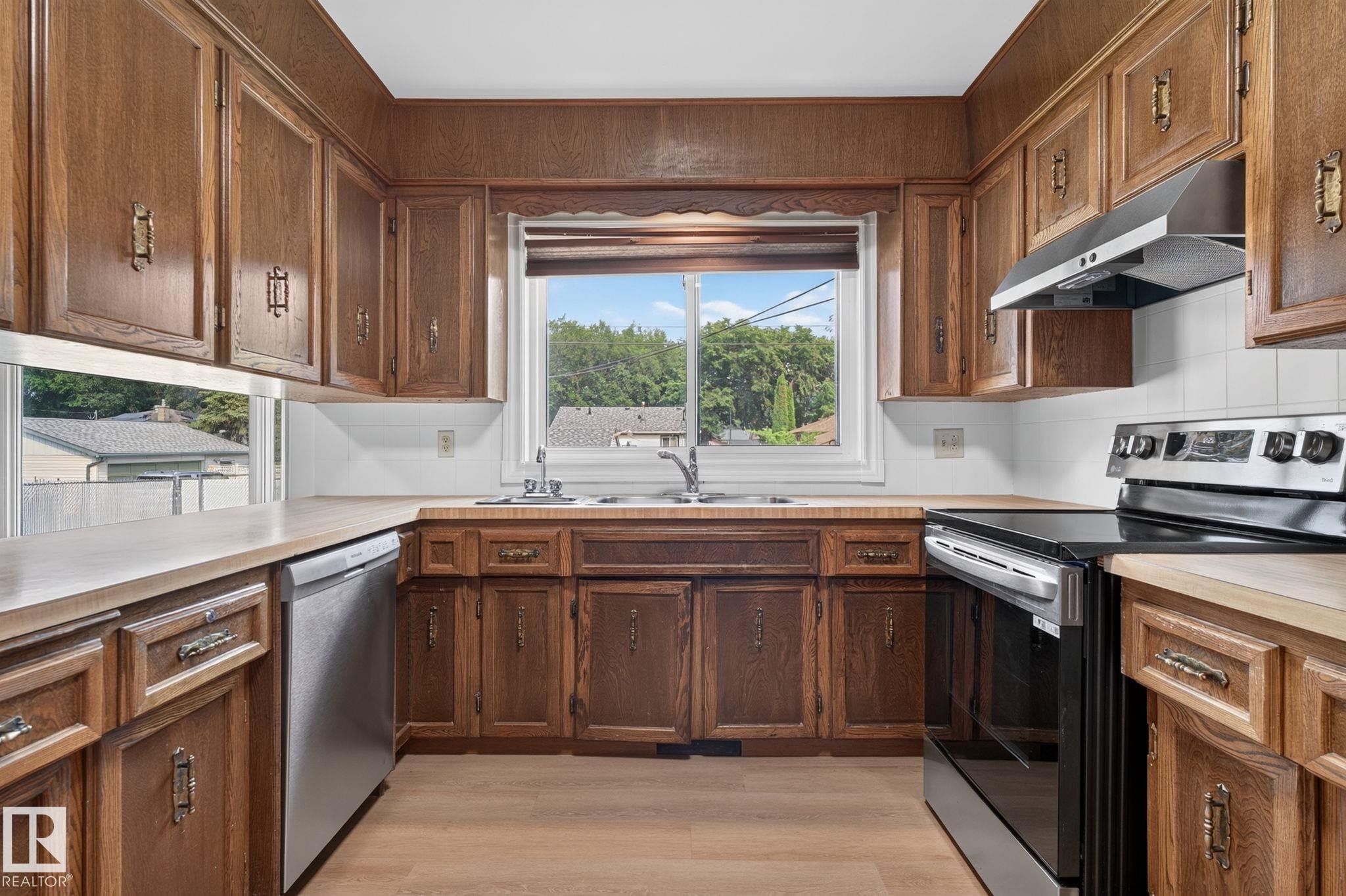 U-shaped kitchen featuring wood cabinetry, stainless steel range with overhead hood, stainless steel dishwasher, and a double basin sink - 12121 42 Street Nw, Edmonton, AB - Indoor Photo Showing Kitchen With Double Sink
