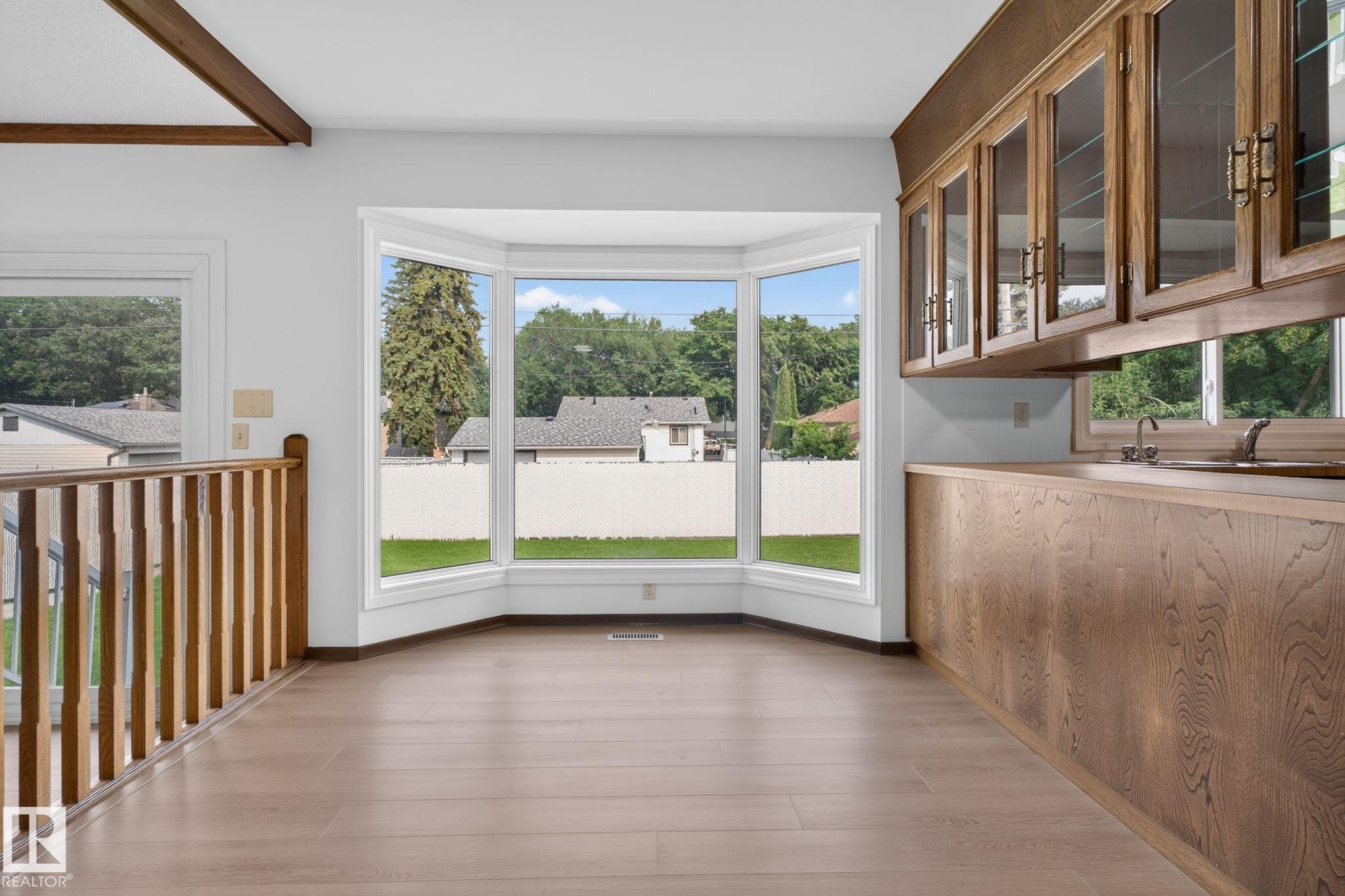 Bay window with white trim, wood-finish flooring, wood cabinetry with glass fronts, wood countertop, and a wood railing with vertical spindles - 12121 42 Street Nw, Edmonton, AB - Indoor Photo Showing Other Room