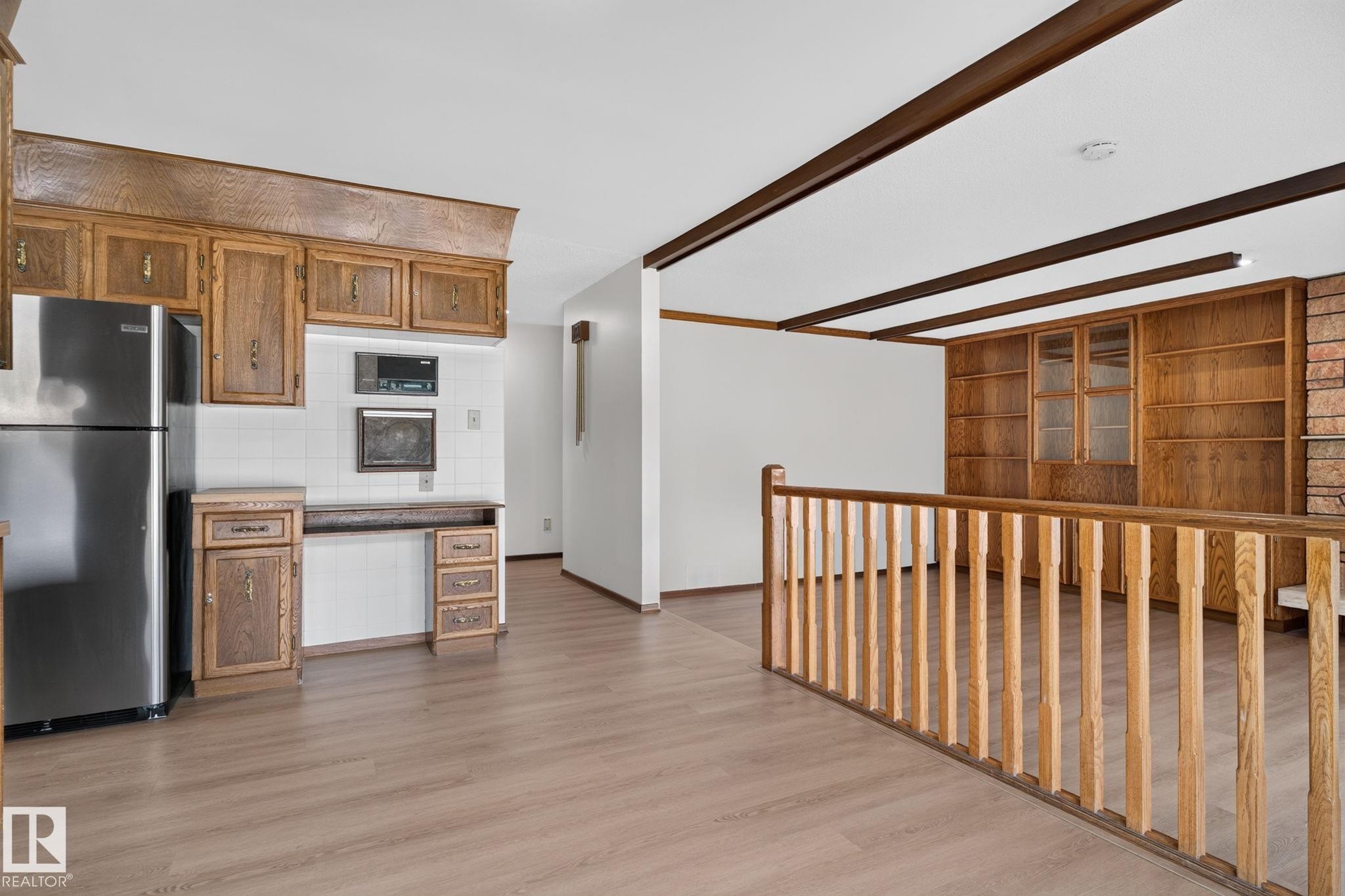Kitchen area featuring wood cabinetry, white tile backsplash, and stainless steel refrigerator - 12121 42 Street Nw, Edmonton, AB - Indoor Photo Showing Kitchen