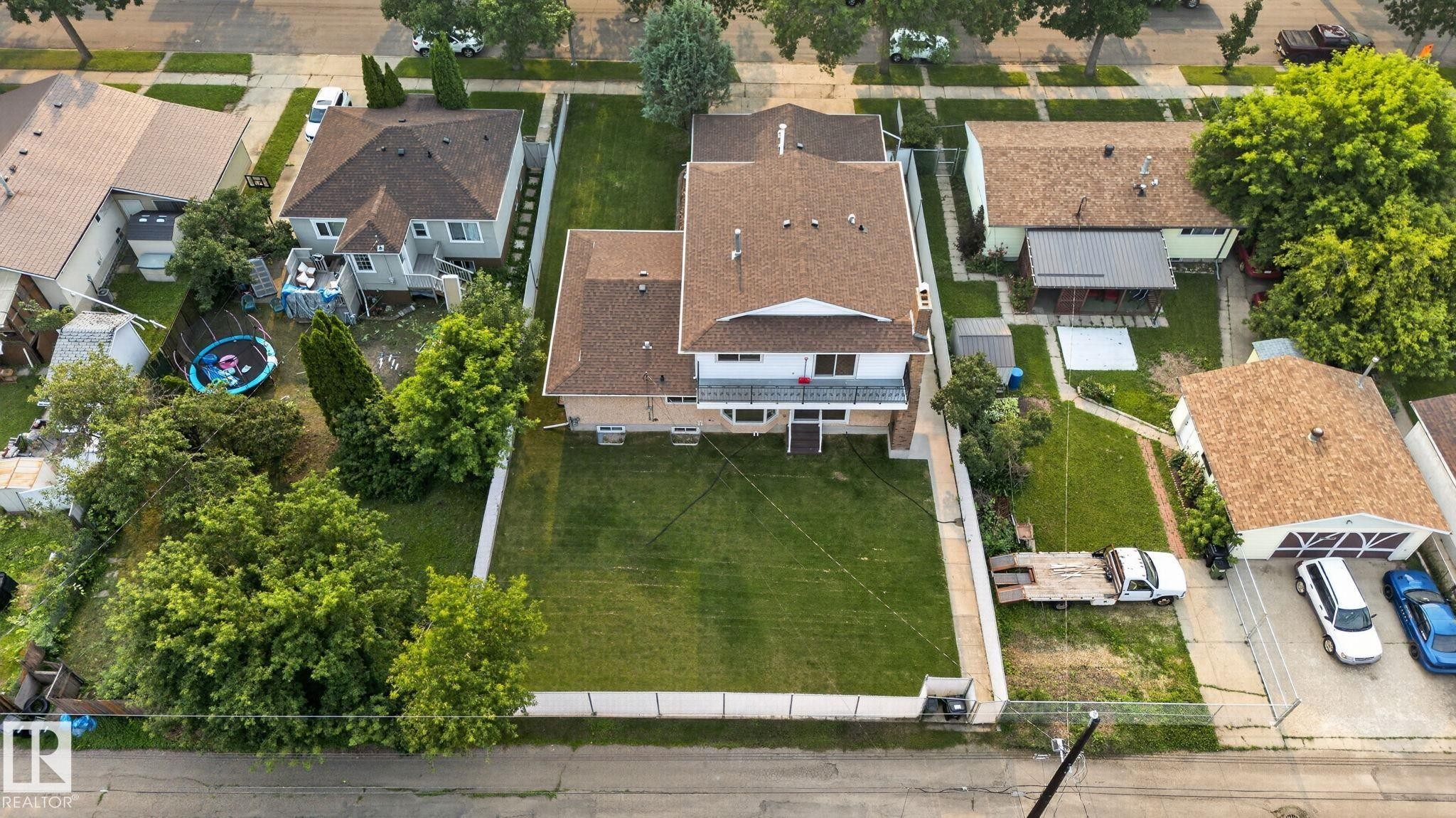 Aerial overview showcasing a property with a spacious backyard, mature trees, and an extended driveway leading to a detached garage - 12121 42 Street Nw, Edmonton, AB - Outdoor