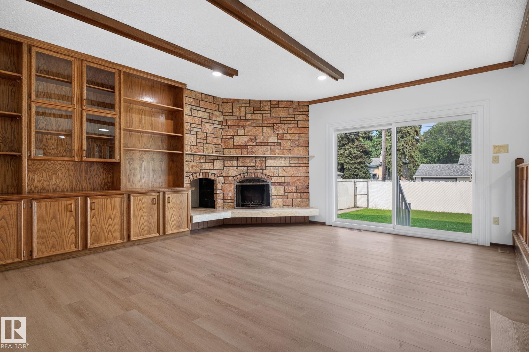 Spacious interior featuring wood-finish flooring, exposed ceiling beams, and a stone-clad fireplace - 12121 42 Street Nw, Edmonton, AB - Indoor With Fireplace