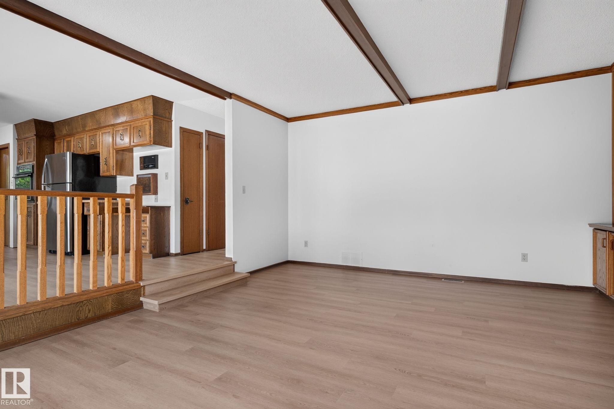 Open-concept living space featuring wood-finish flooring, white walls, and a white ceiling with exposed wood beams - 12121 42 Street Nw, Edmonton, AB - Indoor Photo Showing Other Room