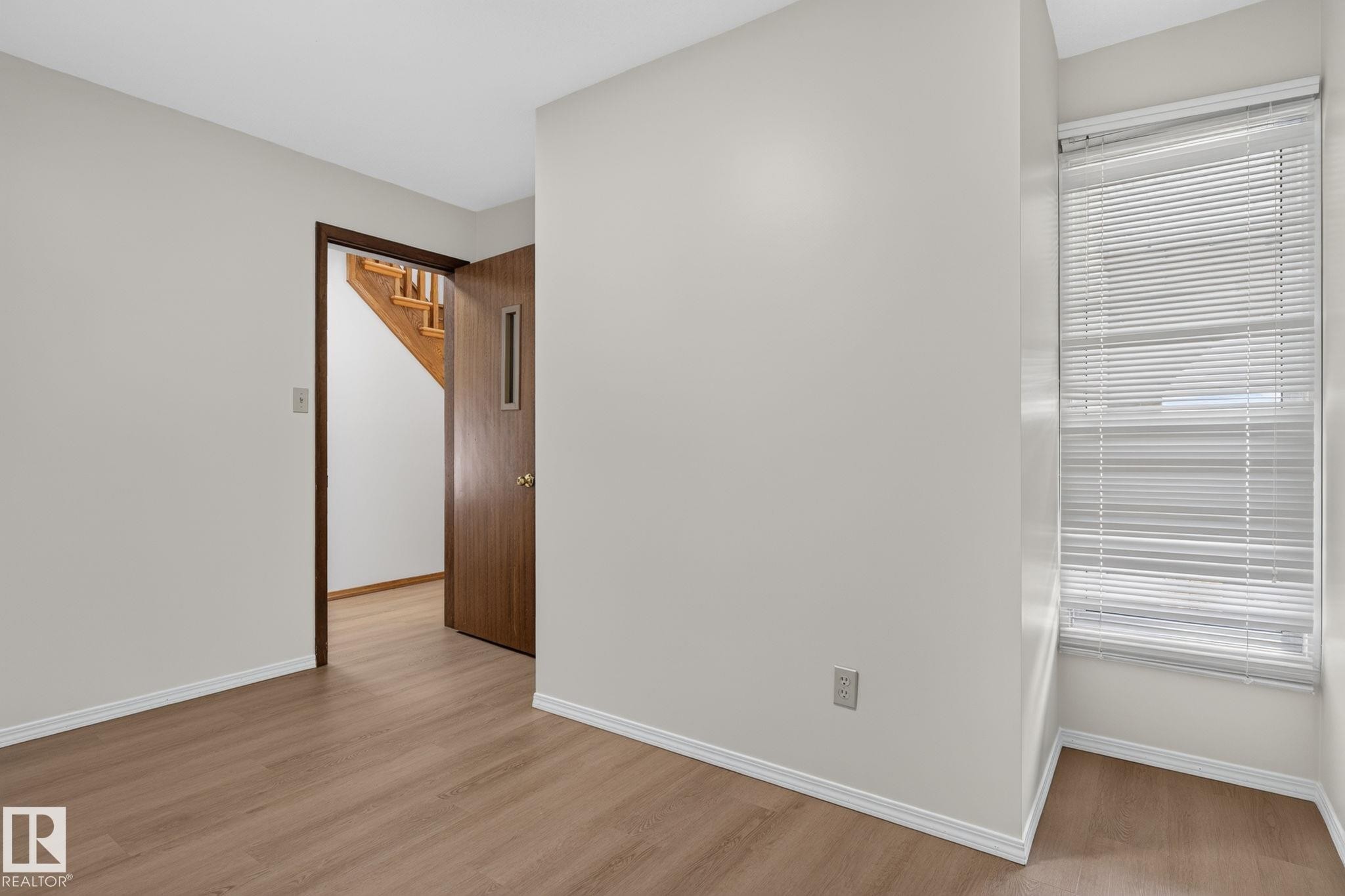 Bright interior space featuring wood-finish flooring, white baseboards, and neutral wall paint - 12121 42 Street Nw, Edmonton, AB - Indoor Photo Showing Other Room