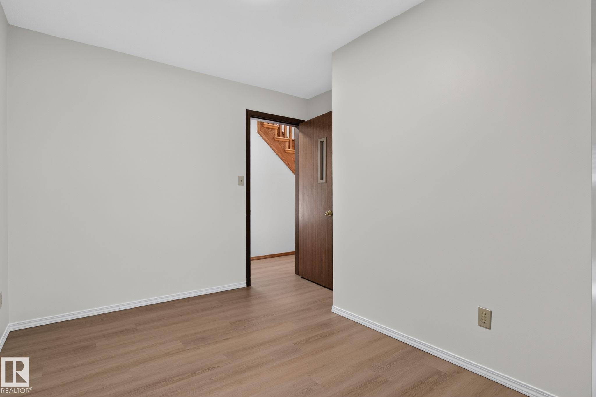 Interior space featuring neutral wall tones, wood-finish flooring, white baseboards, and a brown wood door with a vertical frosted glass insert - 12121 42 Street Nw, Edmonton, AB - Indoor Photo Showing Other Room