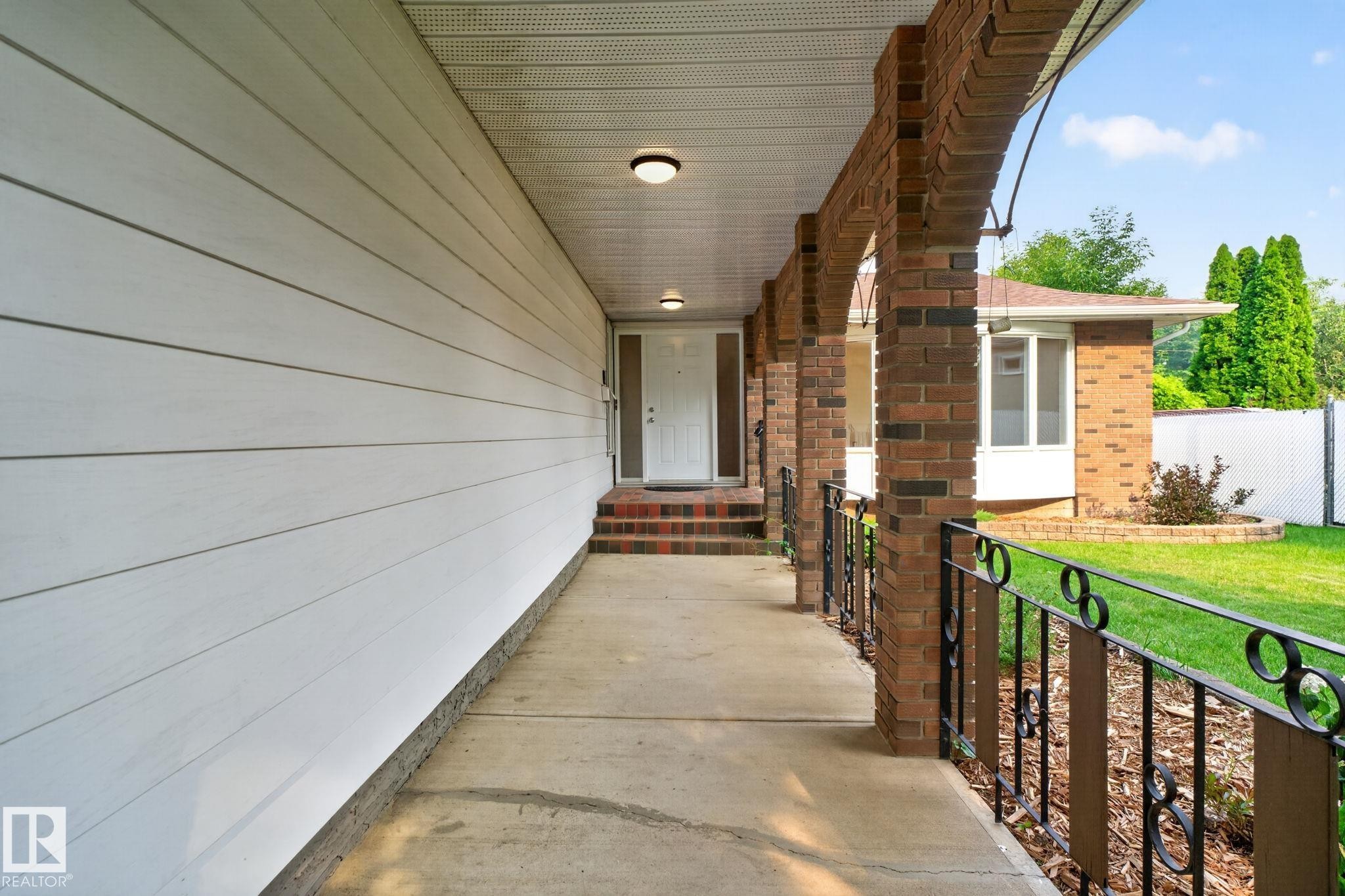 Covered porch entry featuring brick archways and a decorative metal railing - 12121 42 Street Nw, Edmonton, AB - Outdoor With Exterior