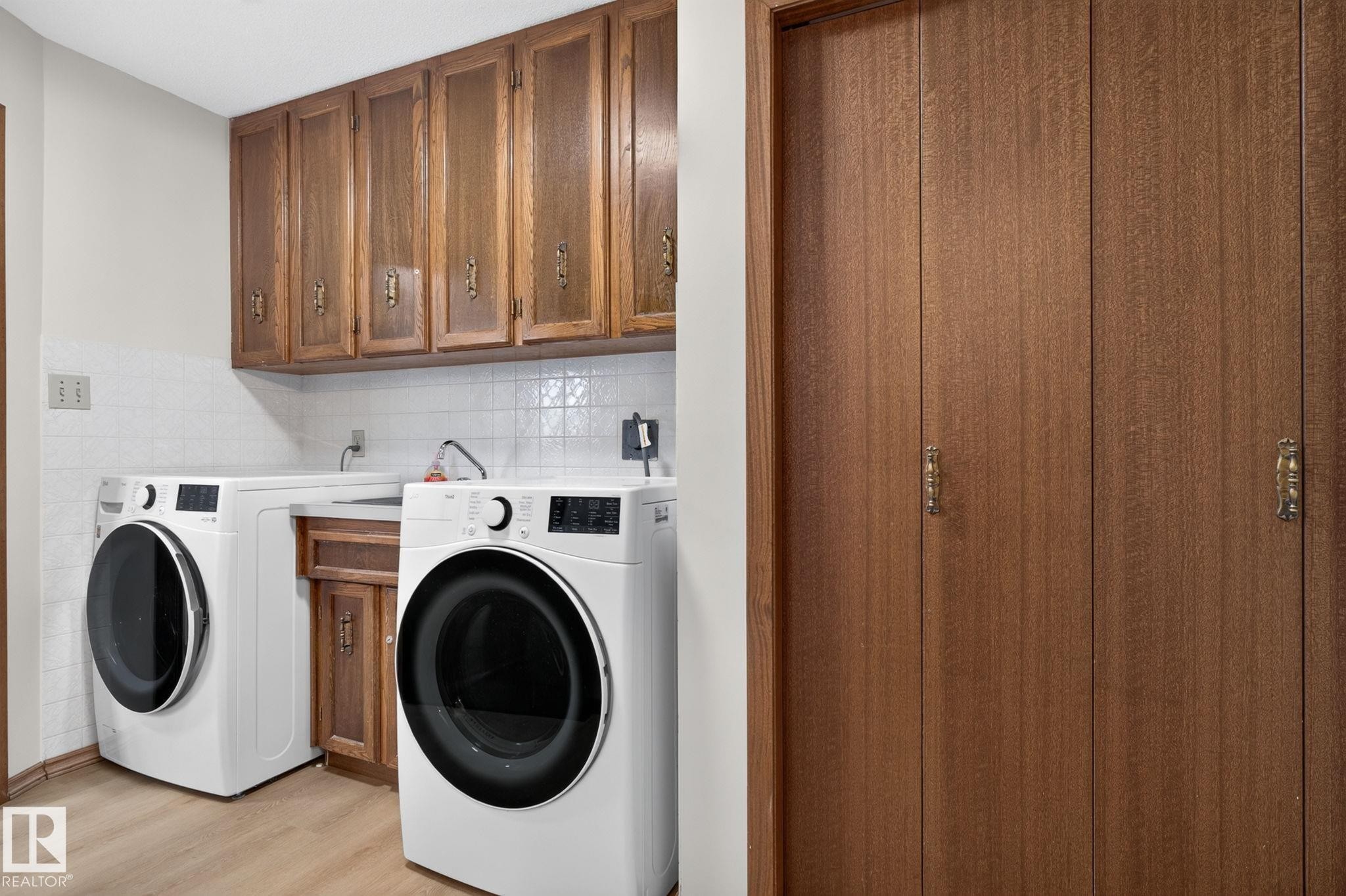Dedicated laundry area featuring abundant cabinetry, a utility sink, and a tiled backsplash - 12121 42 Street Nw, Edmonton, AB - Indoor Photo Showing Laundry Room