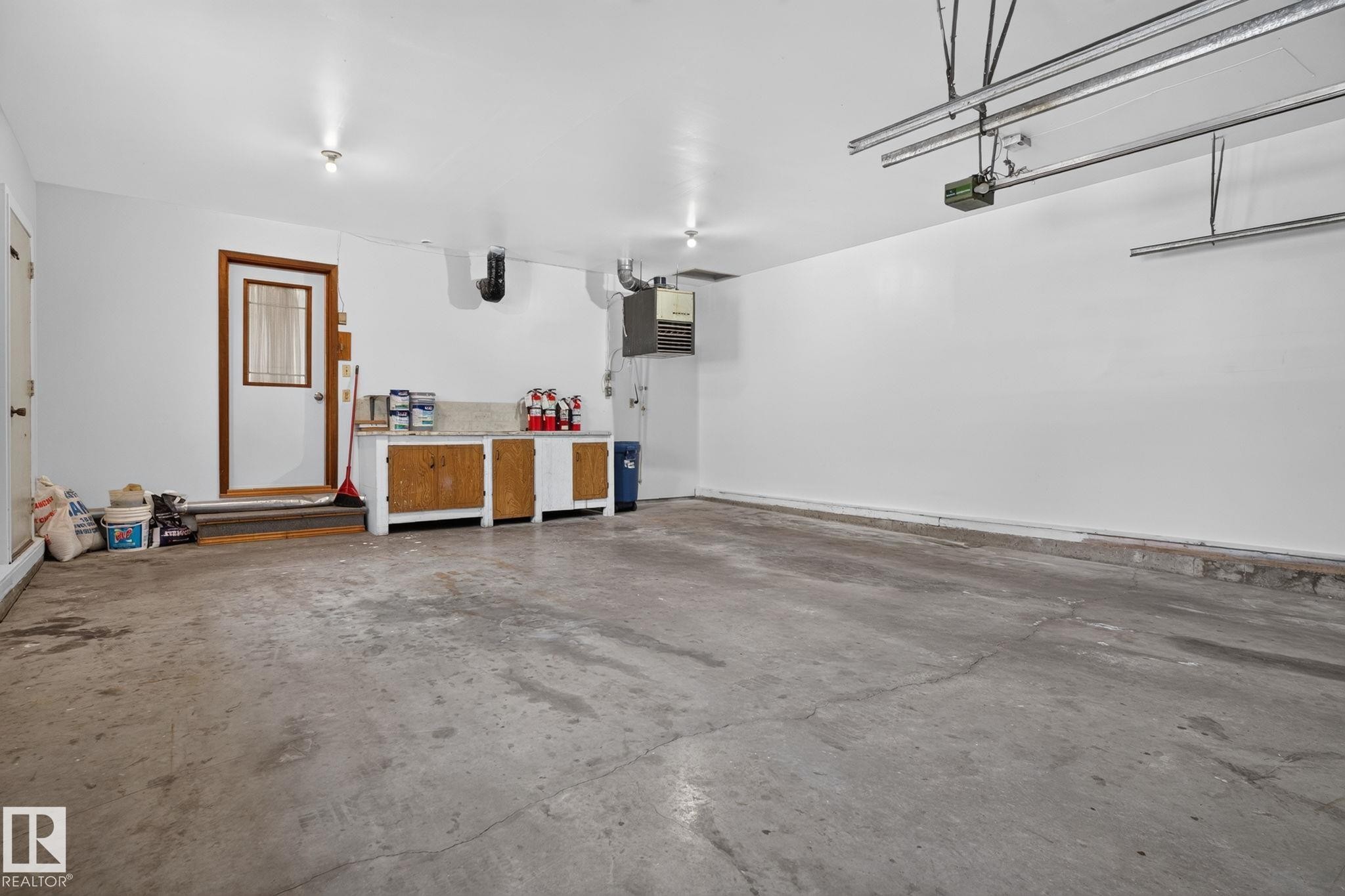 Spacious garage featuring concrete flooring, white walls, built-in cabinetry with a countertop, and an interior access door with a window - 12121 42 Street Nw, Edmonton, AB - Indoor Photo Showing Garage