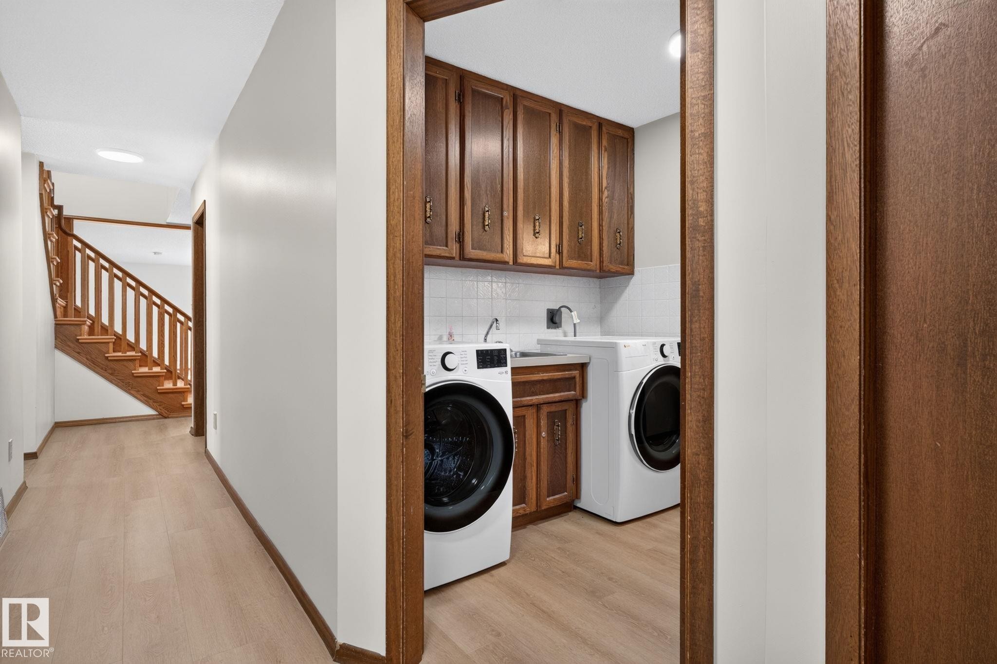 Dedicated laundry area featuring wood cabinetry, white subway tile backsplash, and a utility sink - 12121 42 Street Nw, Edmonton, AB - Indoor Photo Showing Laundry Room