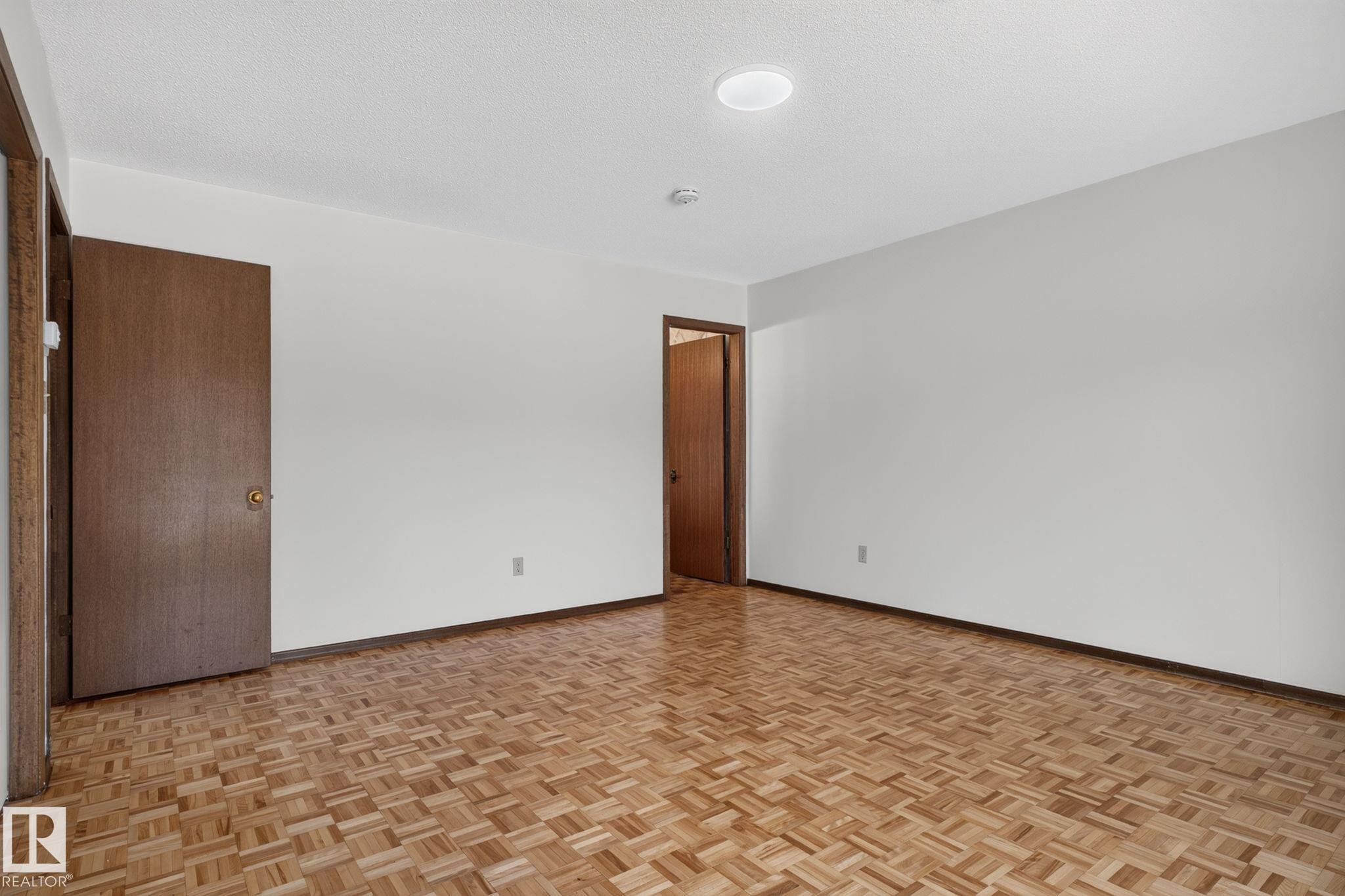 Spacious room featuring wood-finish parquet flooring, white painted walls, and a ceiling-mounted light fixture - 12121 42 Street Nw, Edmonton, AB - Indoor Photo Showing Other Room