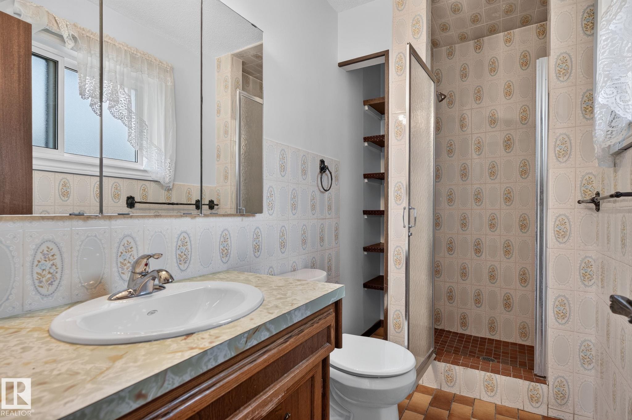 Bathroom featuring a vanity with a drop-in sink, a shower stall with a glass door, a built-in shelving unit, and a window for natural light - 12121 42 Street Nw, Edmonton, AB - Indoor Photo Showing Bathroom