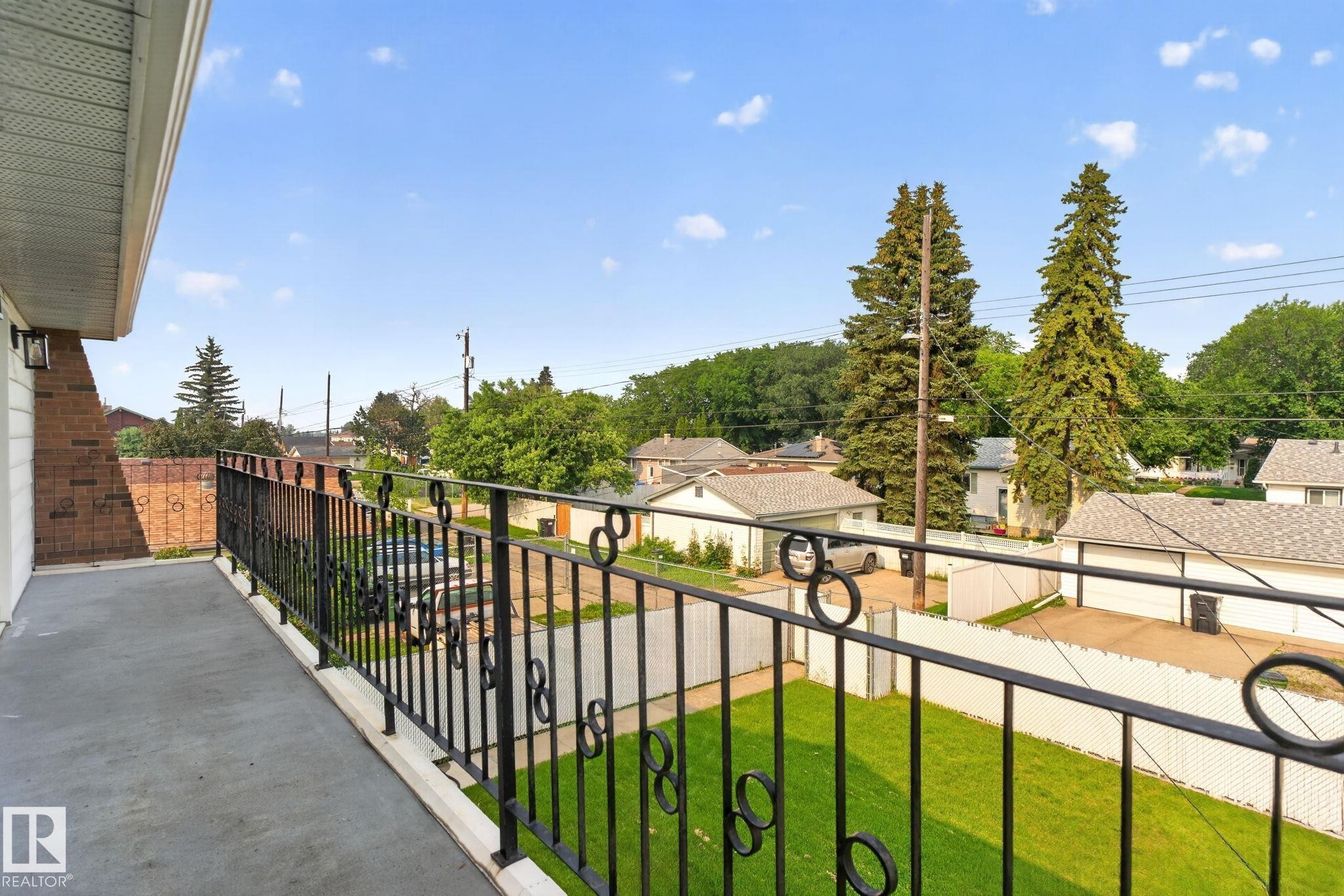 Exterior balcony featuring a wrought iron railing, brick architectural elements, and a concrete surface - 12121 42 Street Nw, Edmonton, AB - Outdoor