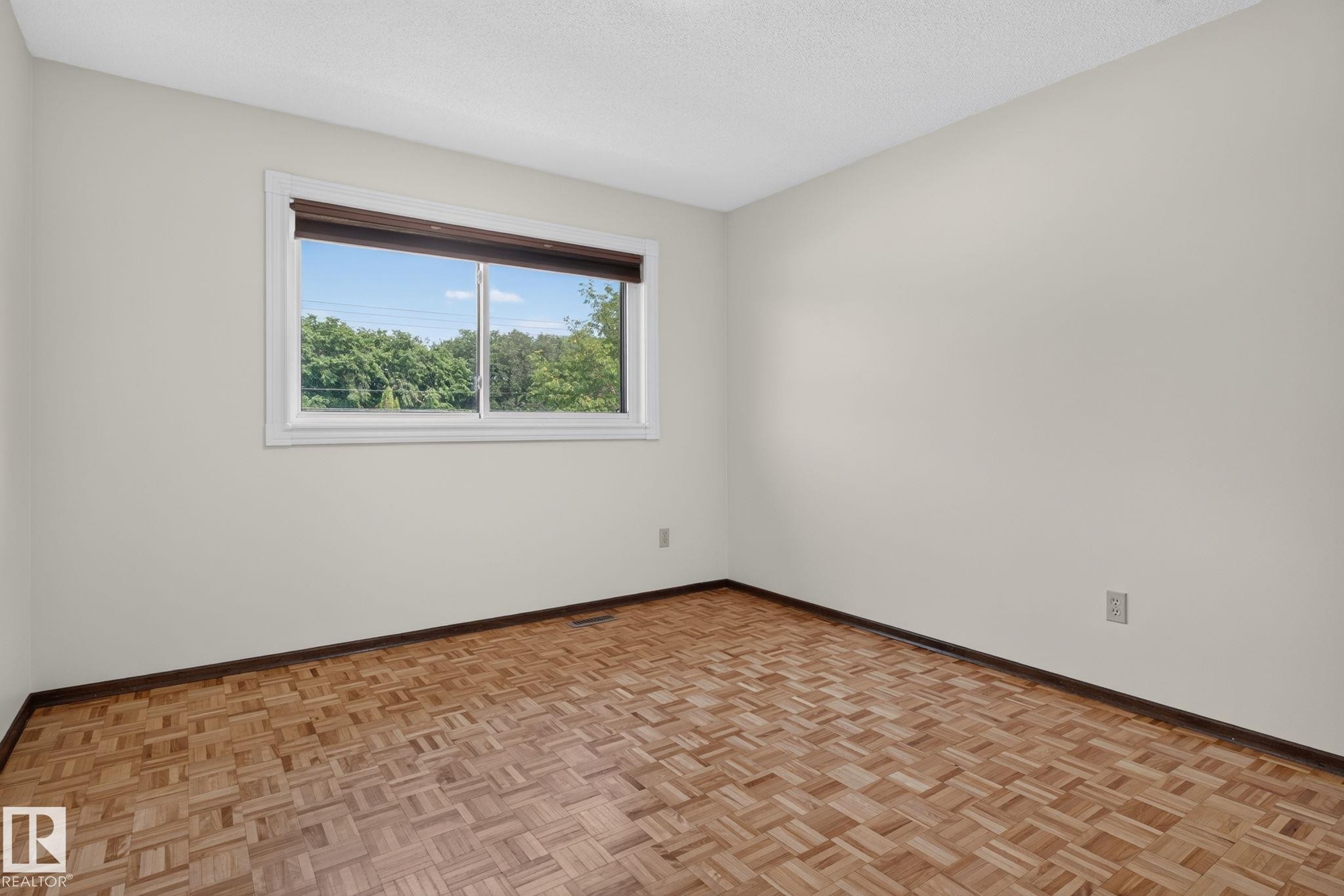 Parquet wood flooring and light-toned walls with a white trim window overlooking green foliage - 12121 42 Street Nw, Edmonton, AB - Indoor Photo Showing Other Room