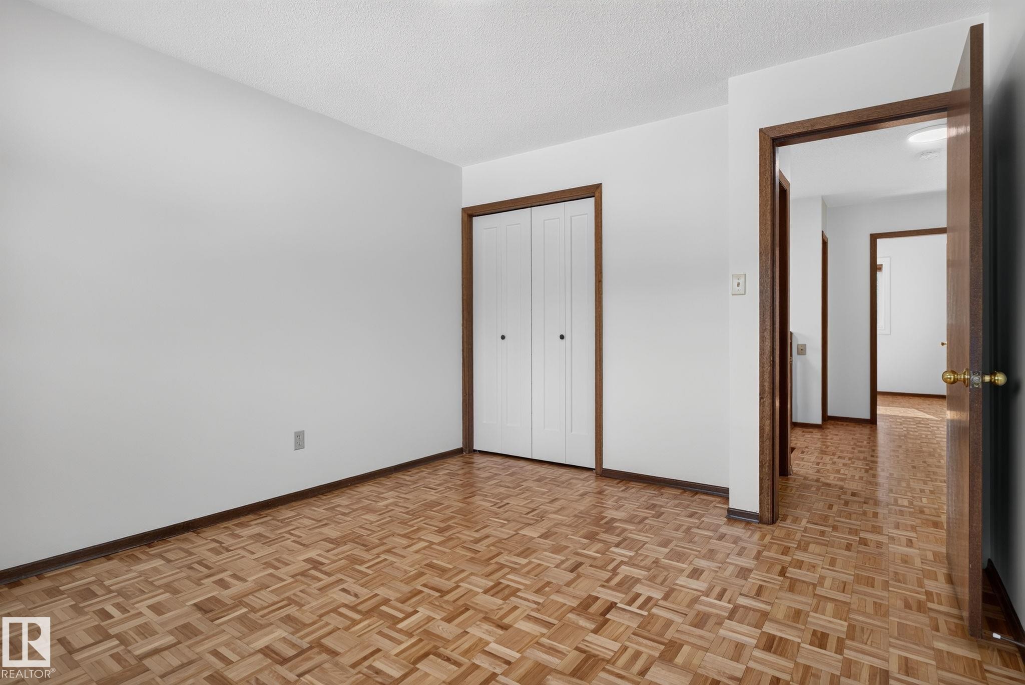Interior room featuring parquet wood flooring, white walls, and a bi-fold closet door with dark trim - 12121 42 Street Nw, Edmonton, AB - Indoor Photo Showing Other Room