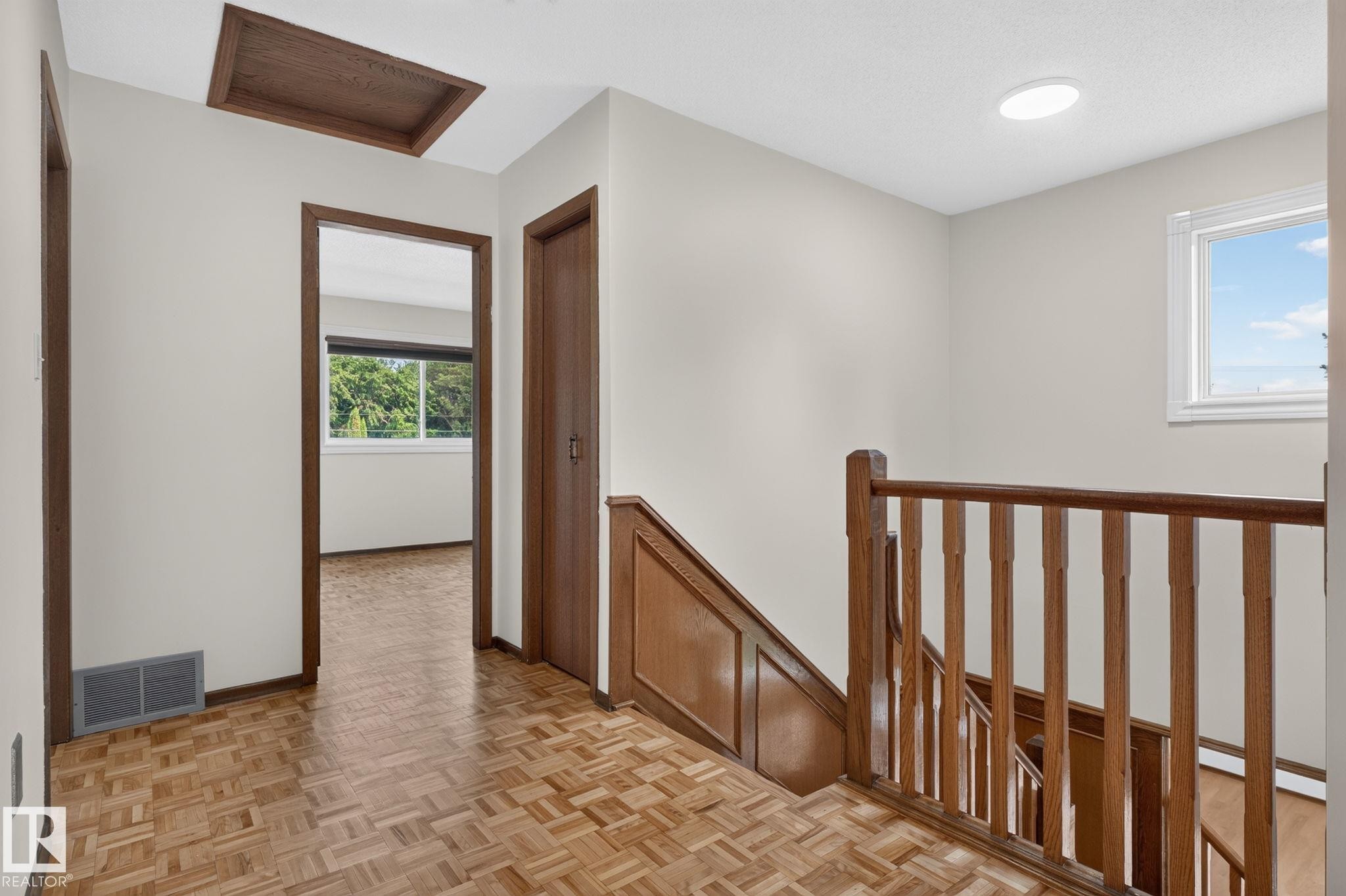 Upper landing with parquet wood-finish flooring, wood-paneled staircase, and bright overhead lighting - 12121 42 Street Nw, Edmonton, AB - Indoor Photo Showing Other Room