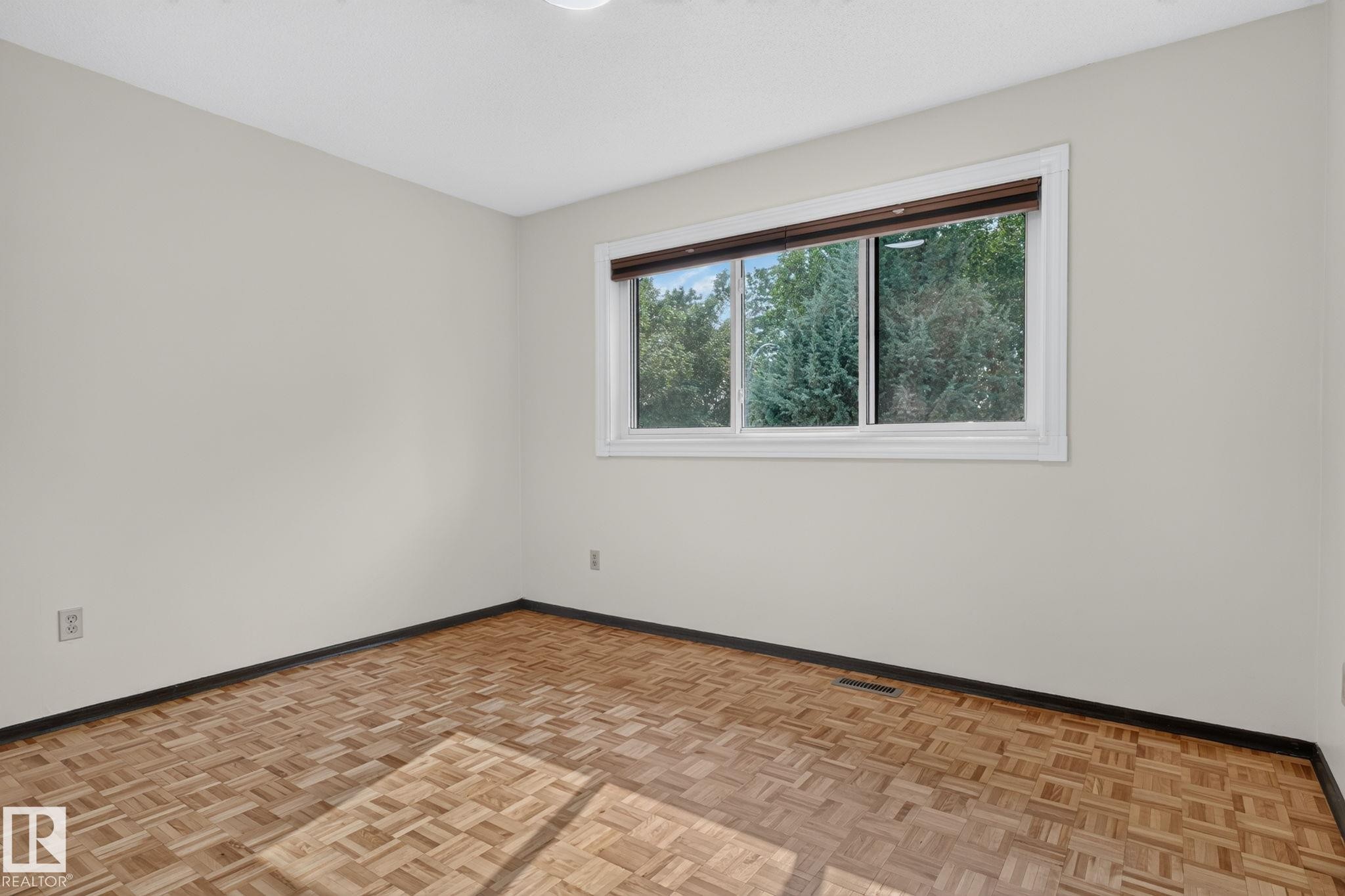 Light-filled room featuring wood-finish parquet flooring, a white trim window with a dark valance, and neutral wall tones - 12121 42 Street Nw, Edmonton, AB - Indoor Photo Showing Other Room