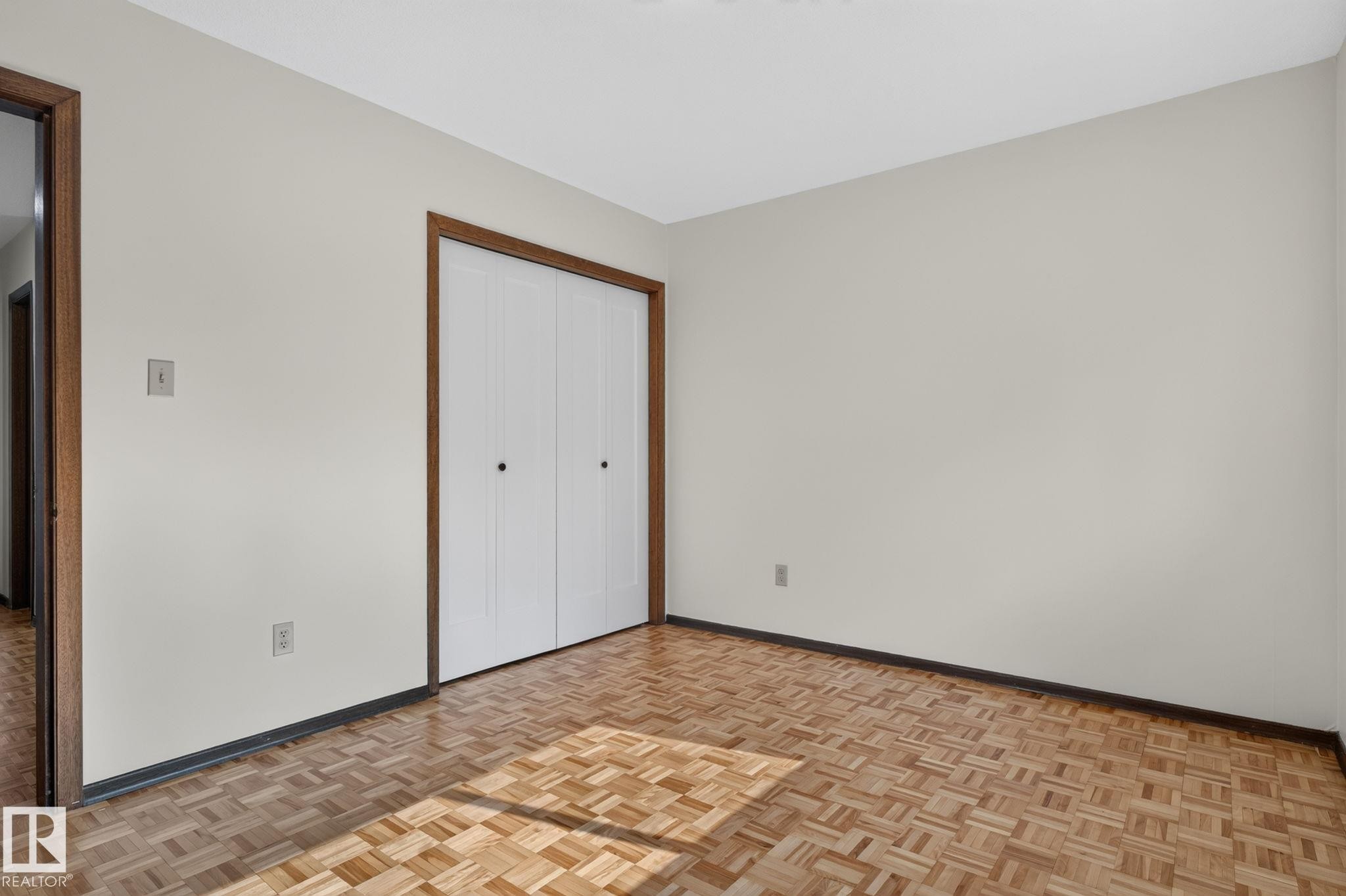 Room featuring wood parquet flooring, white walls, and a built-in bi-fold door closet - 12121 42 Street Nw, Edmonton, AB - Indoor Photo Showing Other Room