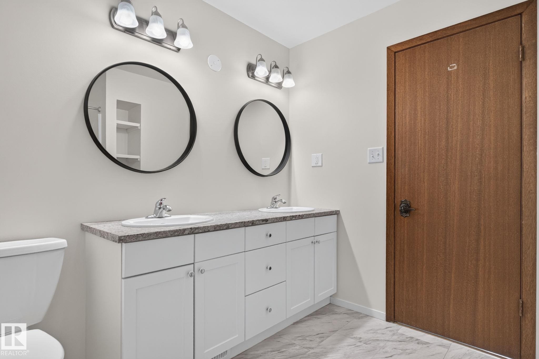 Dual vanity featuring white shaker cabinetry, undermount sinks, and stone-finish countertops - 12121 42 Street Nw, Edmonton, AB - Indoor Photo Showing Bathroom