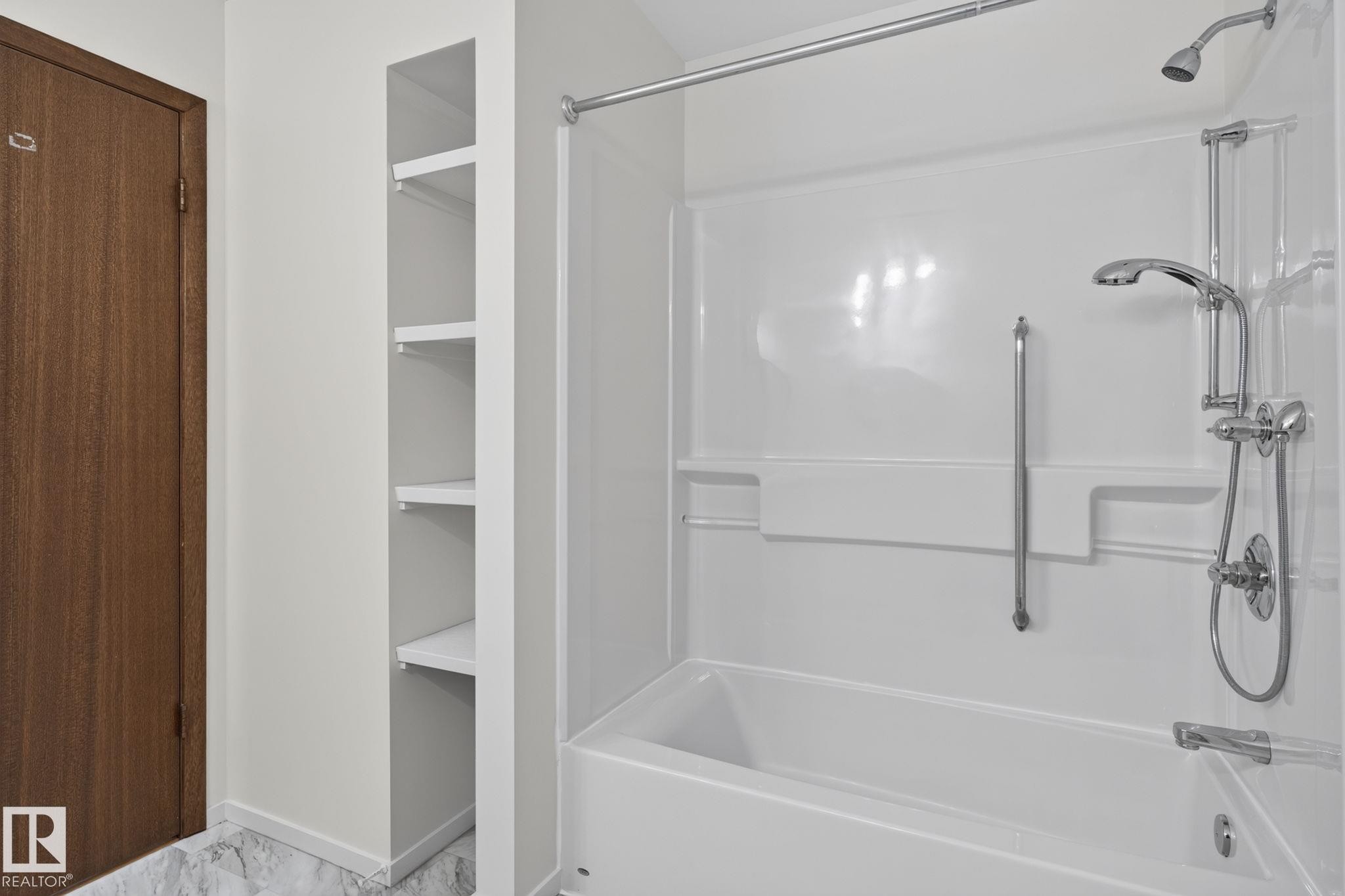 White bathtub and shower combination featuring a multi-function showerhead, an additional shower wand, and a chrome grab bar - 12121 42 Street Nw, Edmonton, AB - Indoor Photo Showing Bathroom