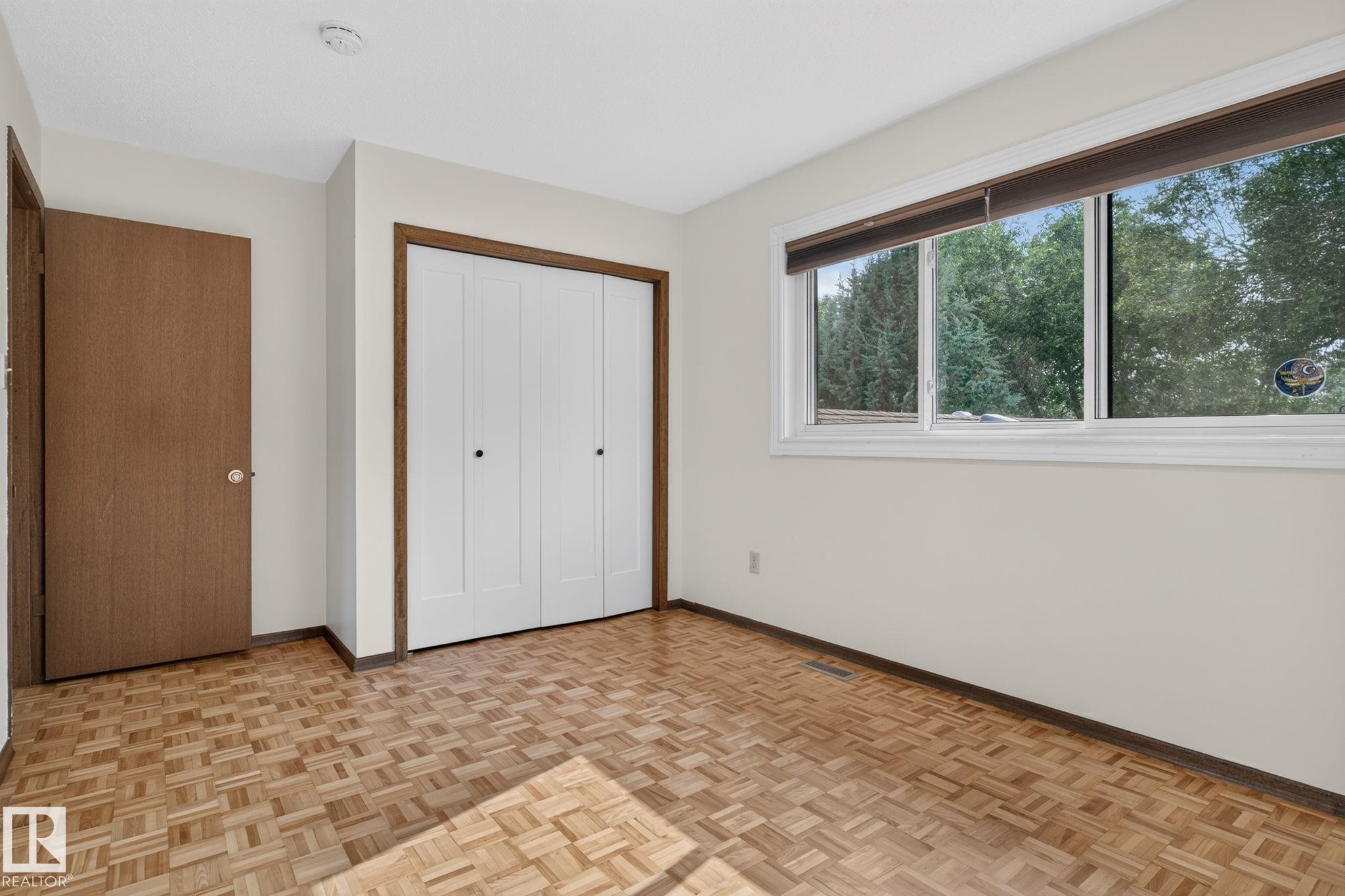 Bright interior space featuring a multi-pane window, wood-finish flooring, a bi-fold closet, and neutral wall tones - 12121 42 Street Nw, Edmonton, AB - Indoor Photo Showing Other Room