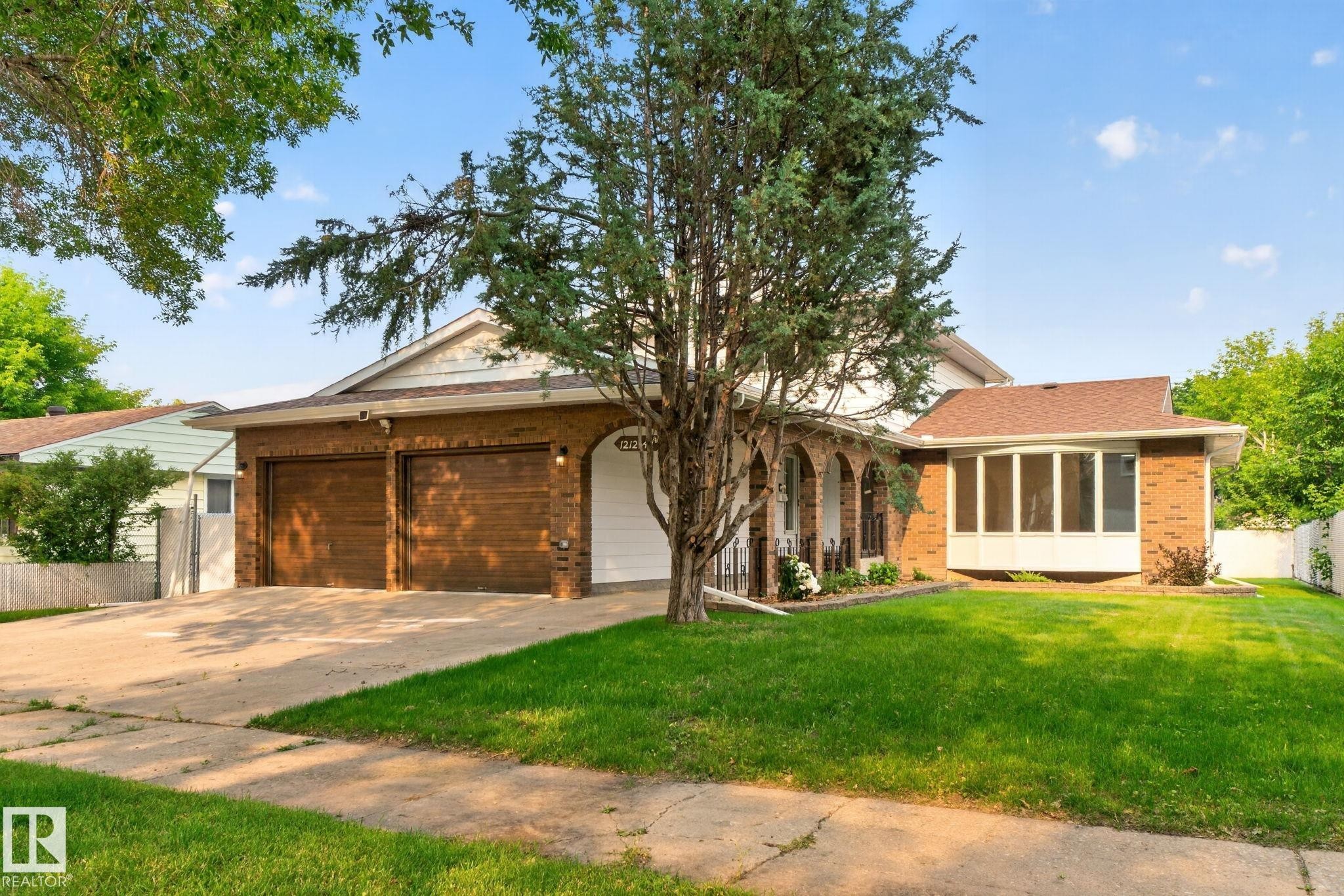Brick-clad exterior featuring a two-car garage with wood-finish doors, an arched entryway, a bay window, and a concrete driveway - 12121 42 Street Nw, Edmonton, AB - Outdoor