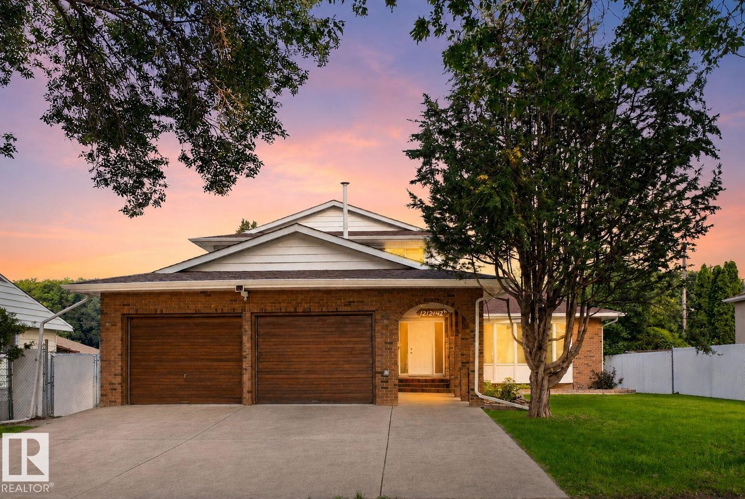 Brick facade residence featuring a two-car garage with wood-finish doors, a concrete driveway, and a manicured front lawn - 12121 42 Street Nw, Edmonton, AB - Outdoor