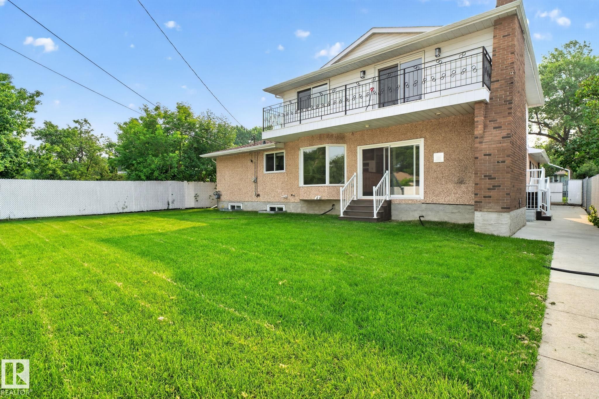 Expansive grassy yard with white perimeter fencing - 12121 42 Street Nw, Edmonton, AB - Outdoor With Balcony