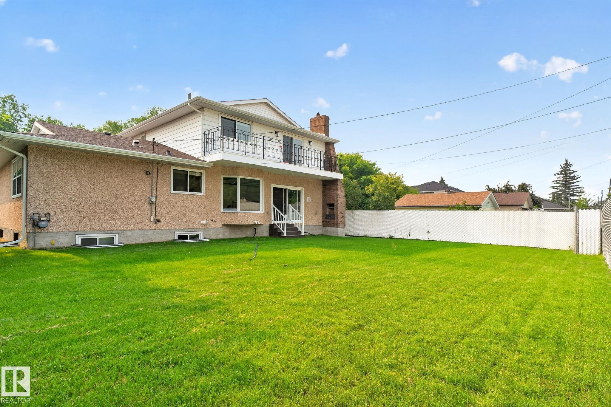 Expansive green lawn with a two-story residence featuring a stucco exterior and a second-story balcony with an ornate metal railing - 12121 42 Street Nw, Edmonton, AB - Outdoor