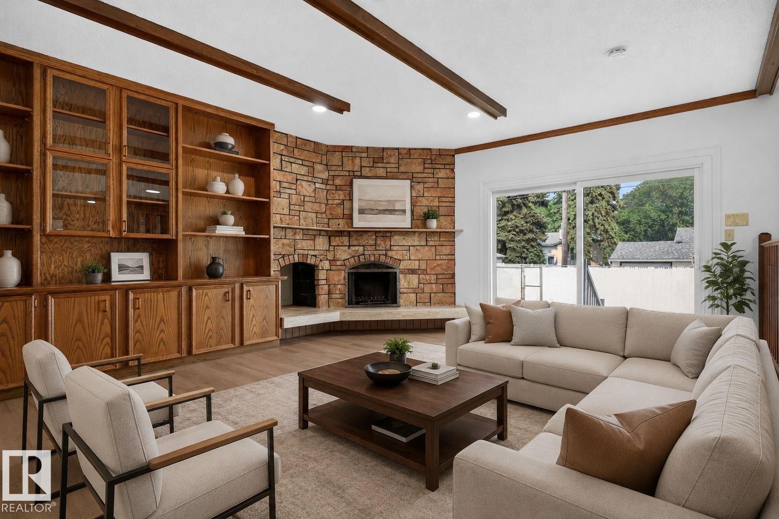Living area featuring a stone-clad fireplace, extensive built-in wooden cabinetry with glass-front uppers, wood-finish flooring, and exposed ceiling beams - 12121 42 Street Nw, Edmonton, AB - Indoor Photo Showing Living Room With Fireplace