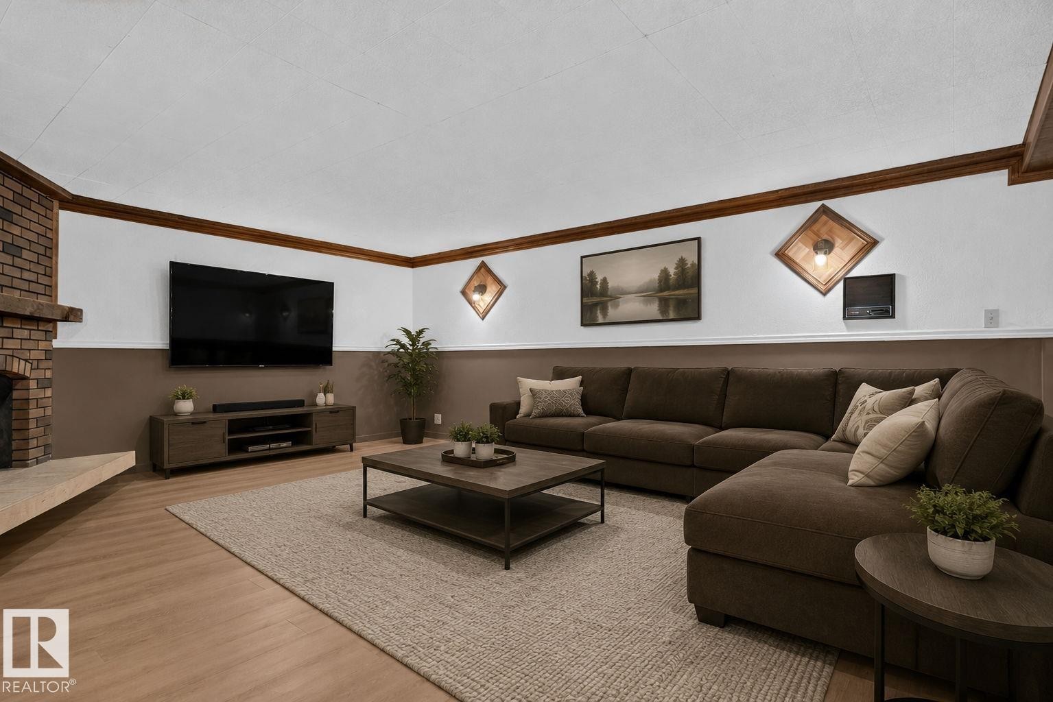 Spacious living area featuring a brick fireplace with a hearth, wood-finish flooring, and crown molding - 12121 42 Street Nw, Edmonton, AB - Indoor Photo Showing Living Room With Fireplace