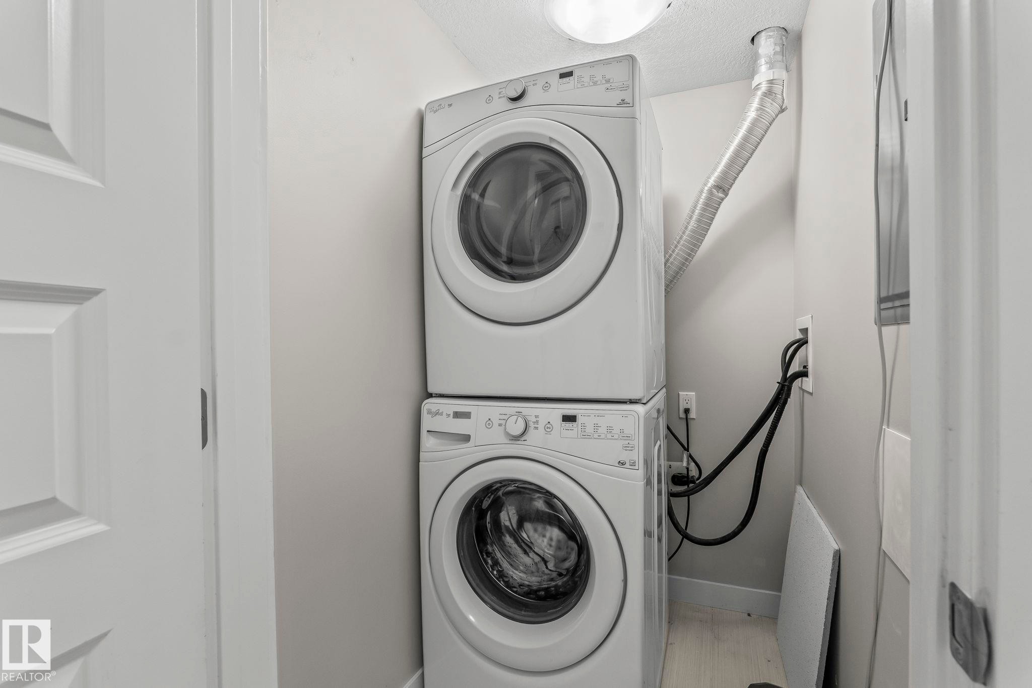 Dedicated laundry area featuring a stacked washer and dryer unit - #324 5151 Windermere Bv Sw, Edmonton, AB - Indoor Photo Showing Laundry Room