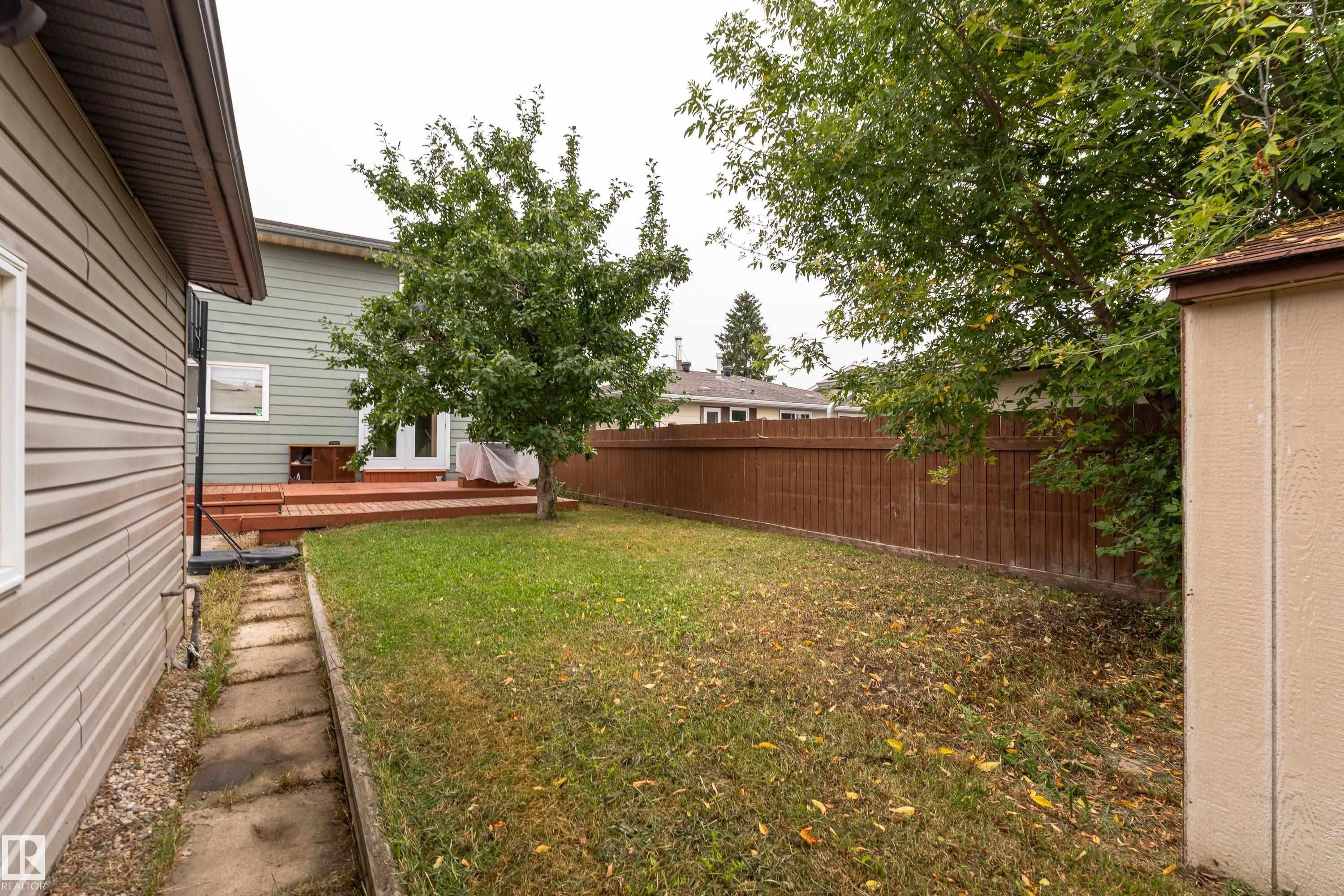 Expansive backyard featuring a manicured lawn, a wooden deck, mature trees, and a privacy fence - 17928 93 Ave Nw, Edmonton, AB
