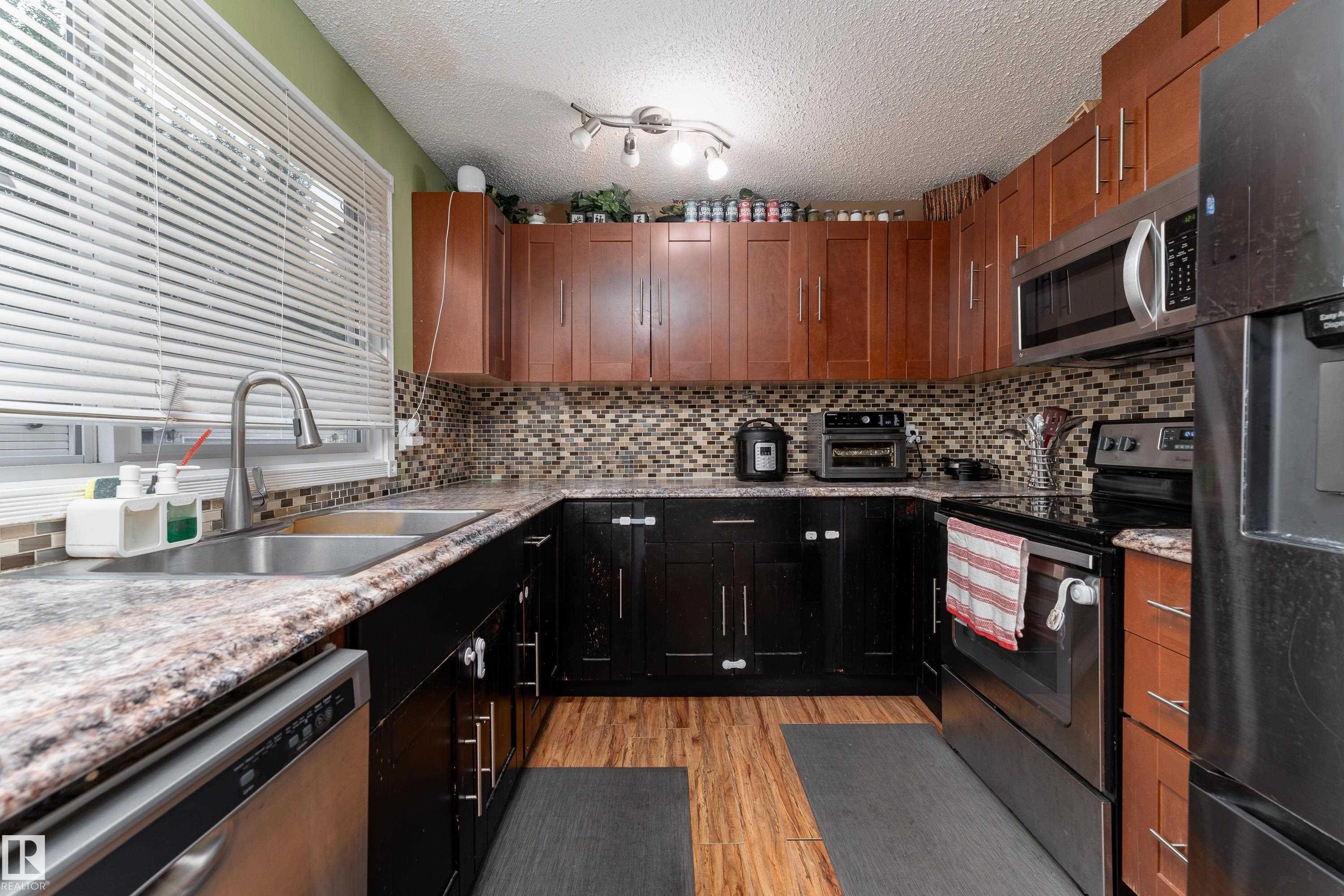 U-shaped kitchen featuring two-tone cabinetry, mosaic tile backsplash, wood-finish flooring, and a stainless steel double basin sink - 17928 93 Ave Nw, Edmonton, AB