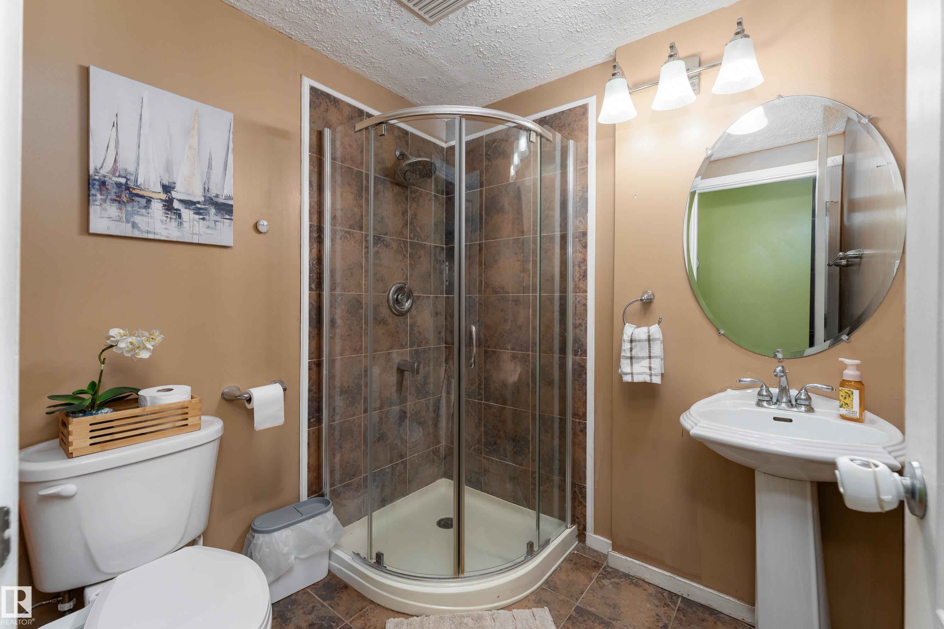 Corner glass shower enclosure with tile surround, pedestal sink with chrome faucet, and a wall-mounted oval mirror - 17928 93 Ave Nw, Edmonton, AB