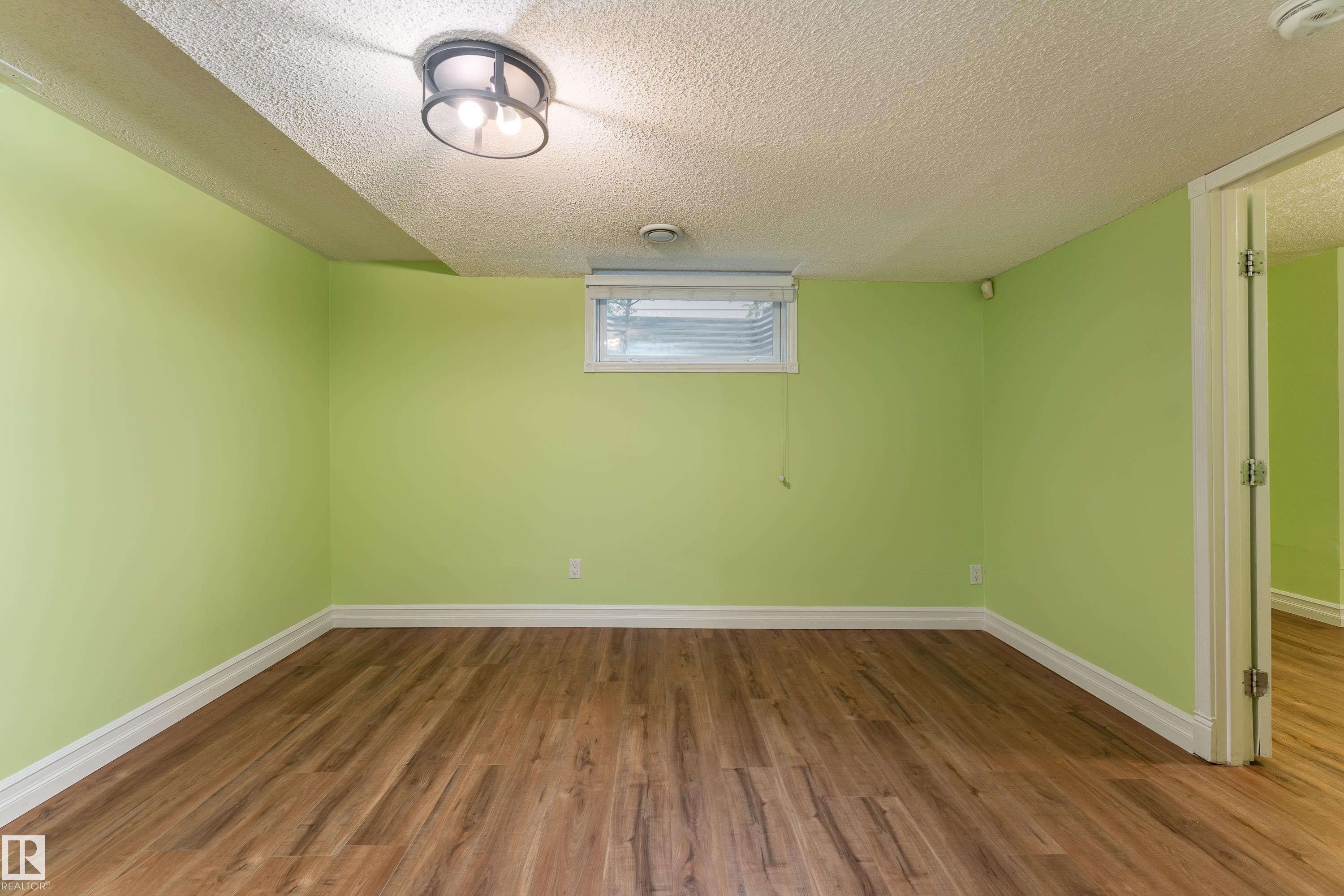 Wood-finish flooring with white trim, a fixed window with blinds, and a modern flush-mount ceiling light - 17928 93 Ave Nw, Edmonton, AB