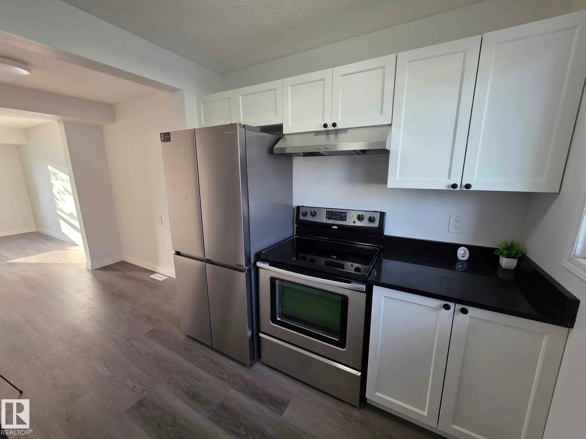 Stainless steel appliances, black countertops, white shaker cabinetry, wood-finish flooring, and recessed lighting - 140 Dickinsfield Court Nw, Edmonton, AB